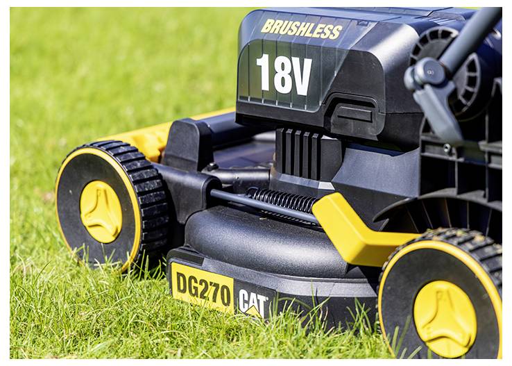 Close-up of a cordless CAT brushless 18V lawn mower resting on grass, showing the front wheels and 'DG270' label.<br>