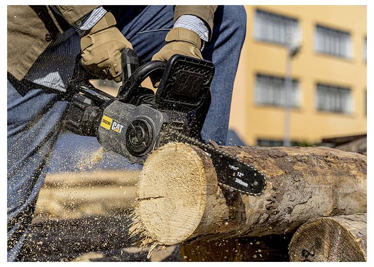 Worker using a chainsaw to cut through a large log outdoors, with wood chips flying.