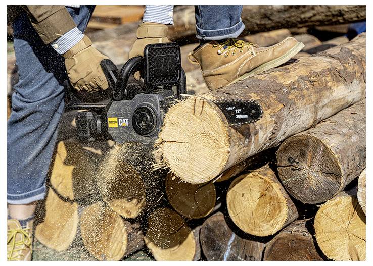 Person uses a chainsaw to cut a log into stacked firewood, with wood chips flying.