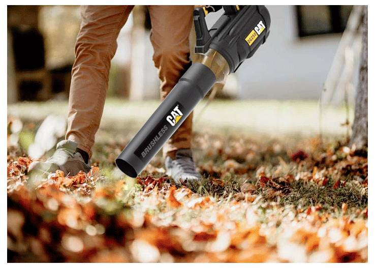 Person using a CAT cordless leaf blower to clear fallen leaves from a yard in autumn.