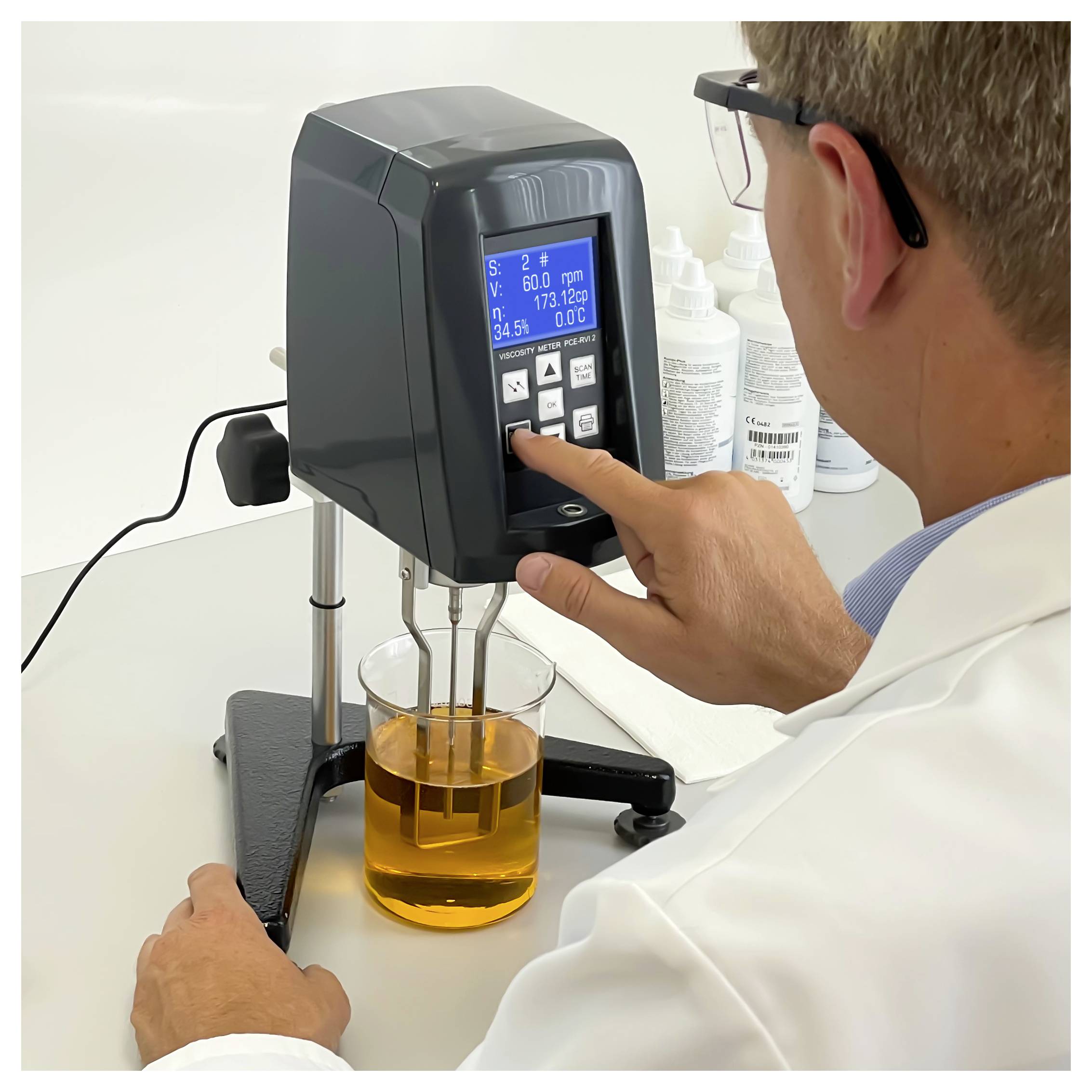 Scientist operating a digital viscometer, lowering a spindle into an amber liquid in a beaker during a lab test.