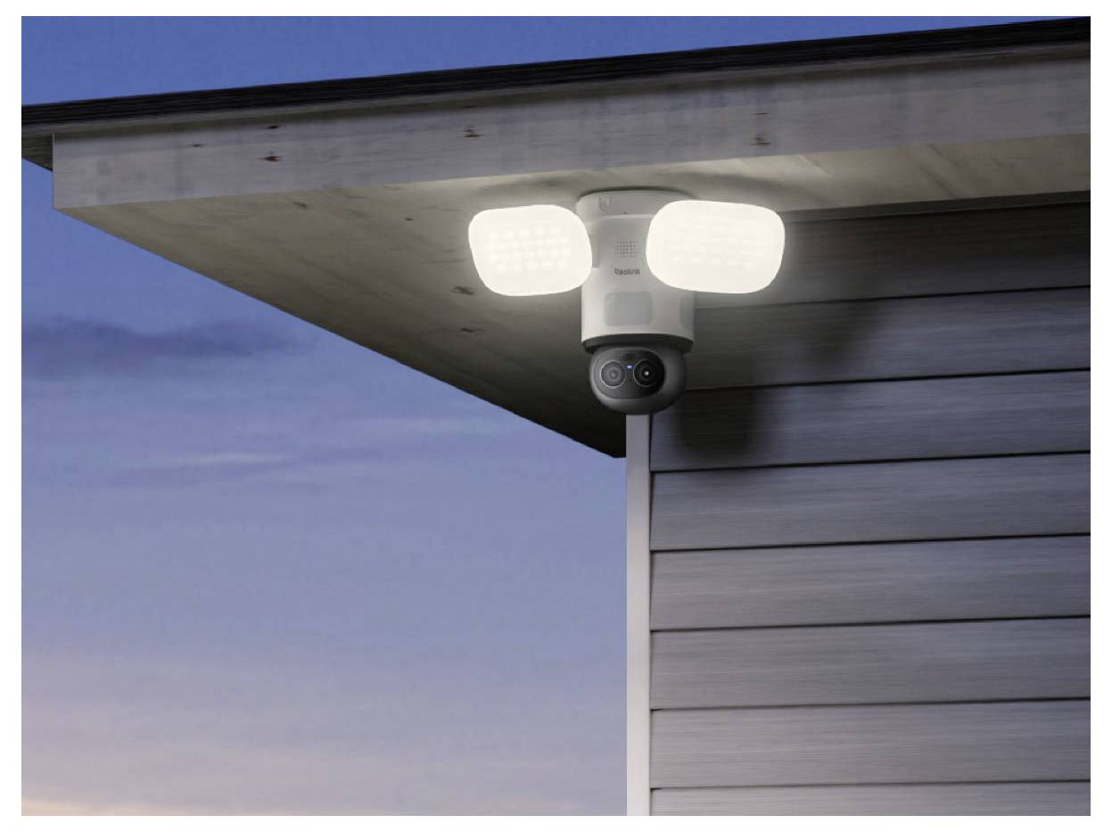 Outdoor security camera with two bright motion-sensor lights mounted under a house eave at dusk.