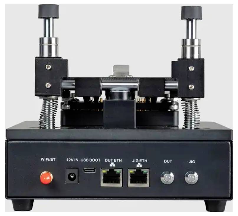 Front view of a black electronic test jig/device with two vertical spring-loaded clamps, a red power button, USB and Ethernet ports, and labeled DUT/JIG connectors.
