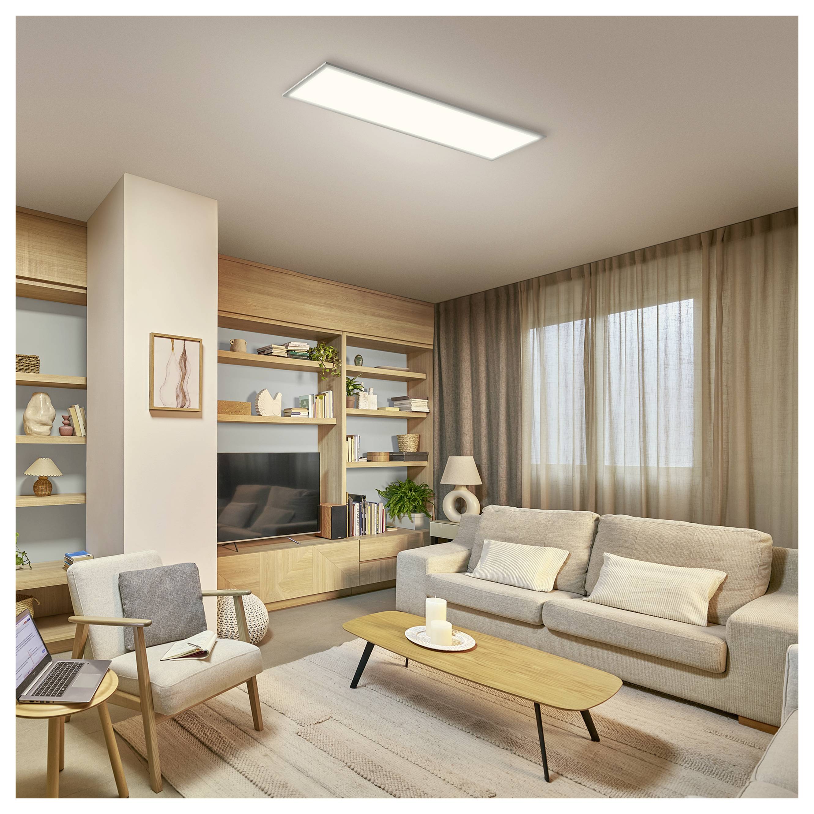 Modern living room with beige sofa, armchair, coffee table, built-in shelves, TV, and a large window with sheer curtains.<br>