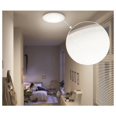 Bedroom at dusk with a person on the bed and a ceiling light shown in a magnified inset, highlighting its soft glow.