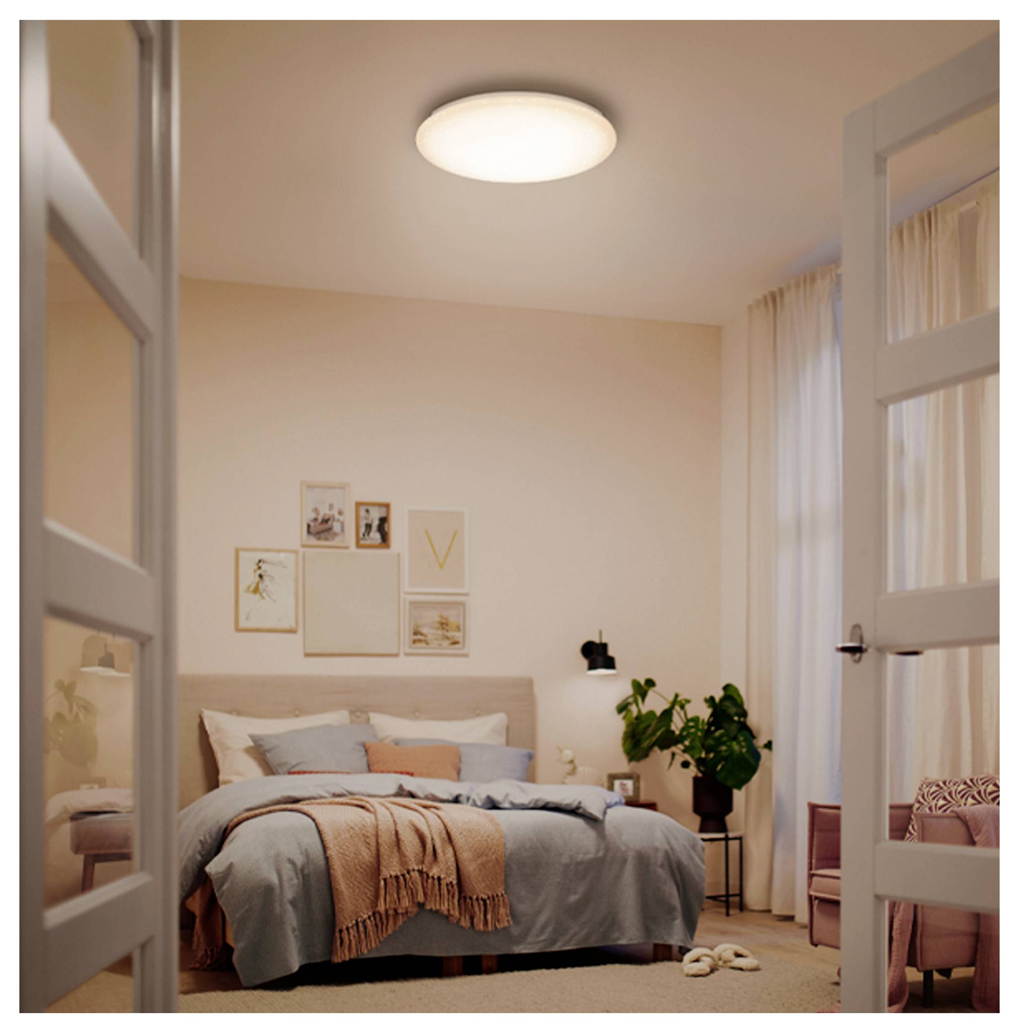 Cozy bedroom seen through open doors, with a neatly made bed, framed wall art, plants, curtains, and soft ceiling light.