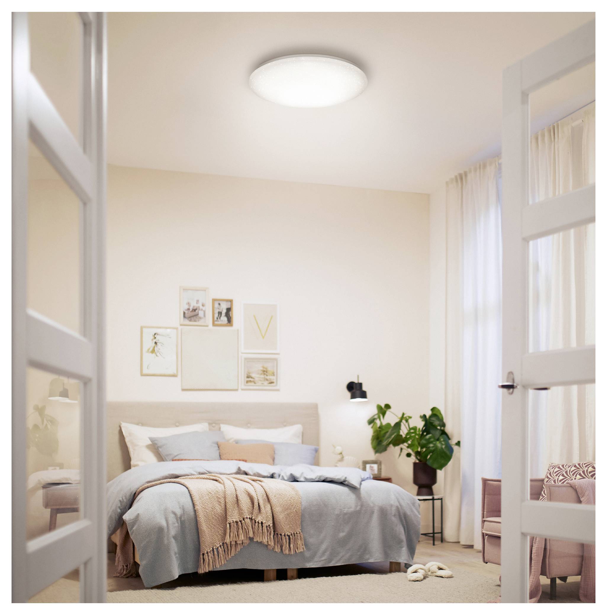Cozy bedroom with neatly made bed, framed wall art, potted plant, and open French doors leading into the room.