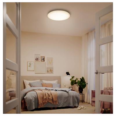 Bright minimalist bedroom with a made bed, wall art, side table plant, curtains, and open double doors viewed from the doorway.