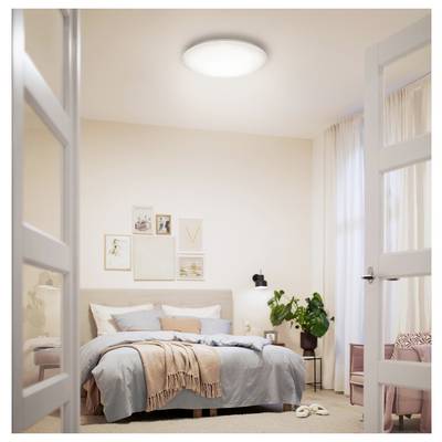 Bright, minimalist bedroom with a neatly made bed, framed wall art, bedside lamp, plant, and open French doors<br>