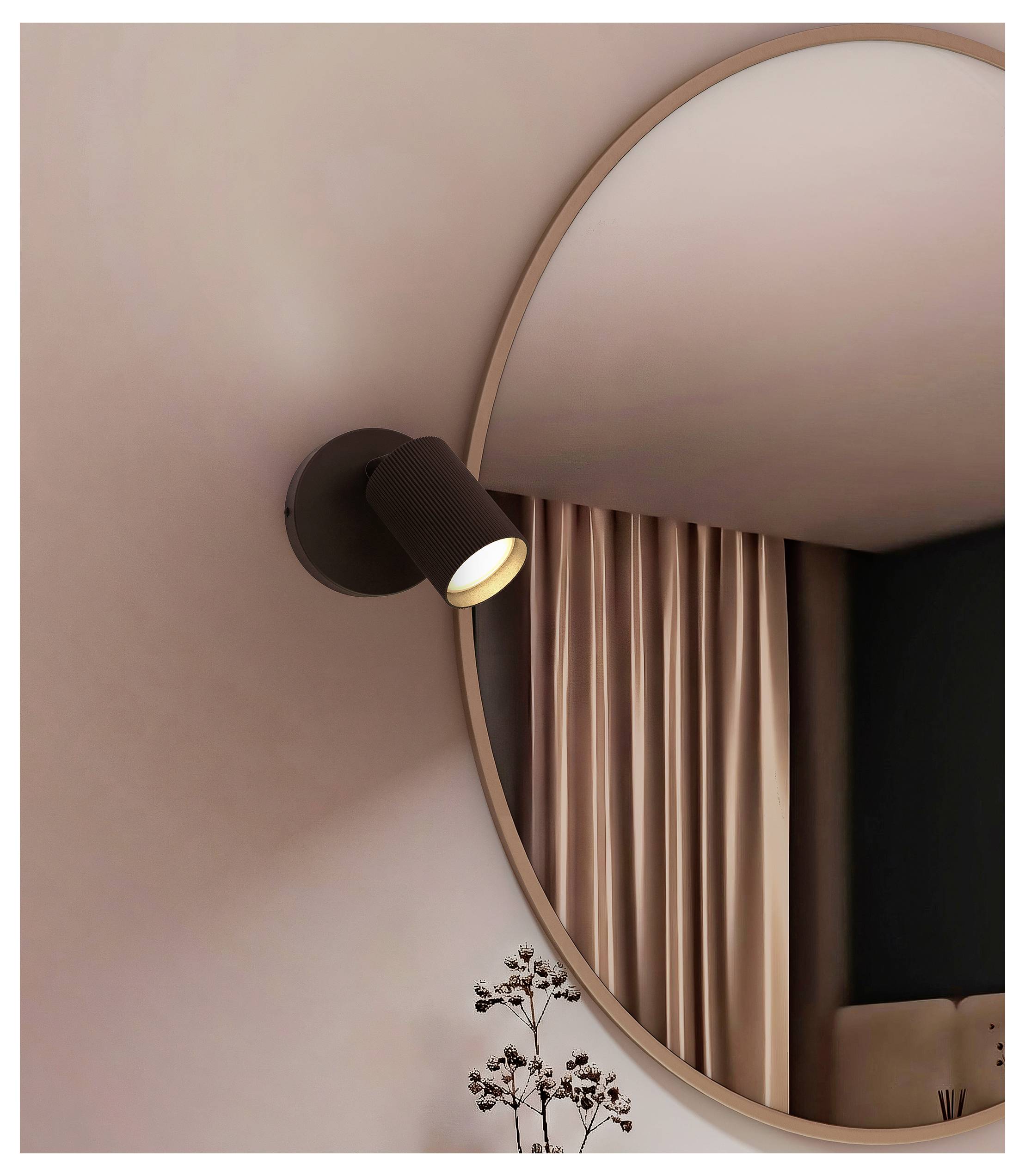 Modern wall sconce with a black spotlight beside a large round mirror reflecting pink curtains in a minimalist room.