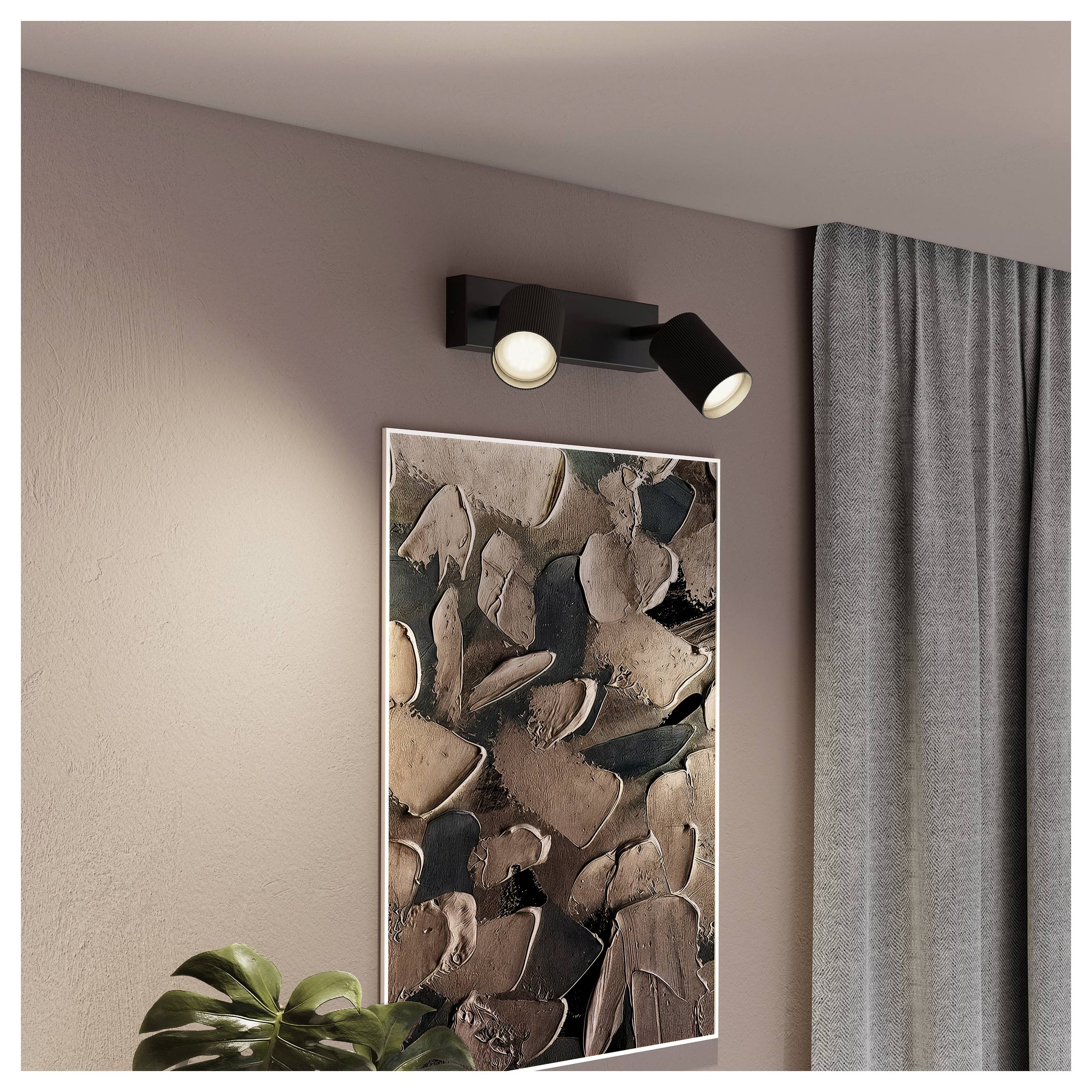 Wall-mounted black dual spotlight above an abstract framed artwork on a beige wall beside gray curtains.