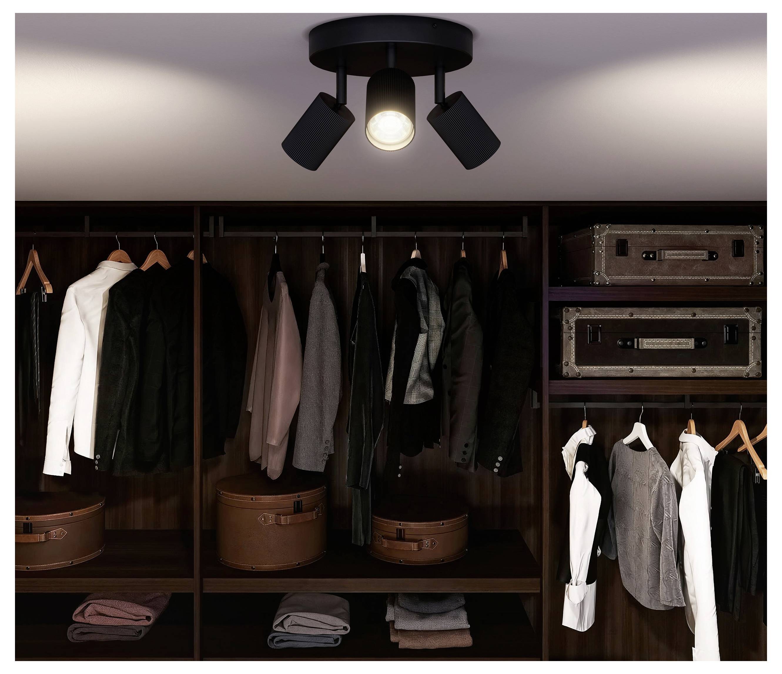 Walk-in closet with dark wood shelving, hanging jackets and shirts, folded clothes, suitcases, and a ceiling spotlight.