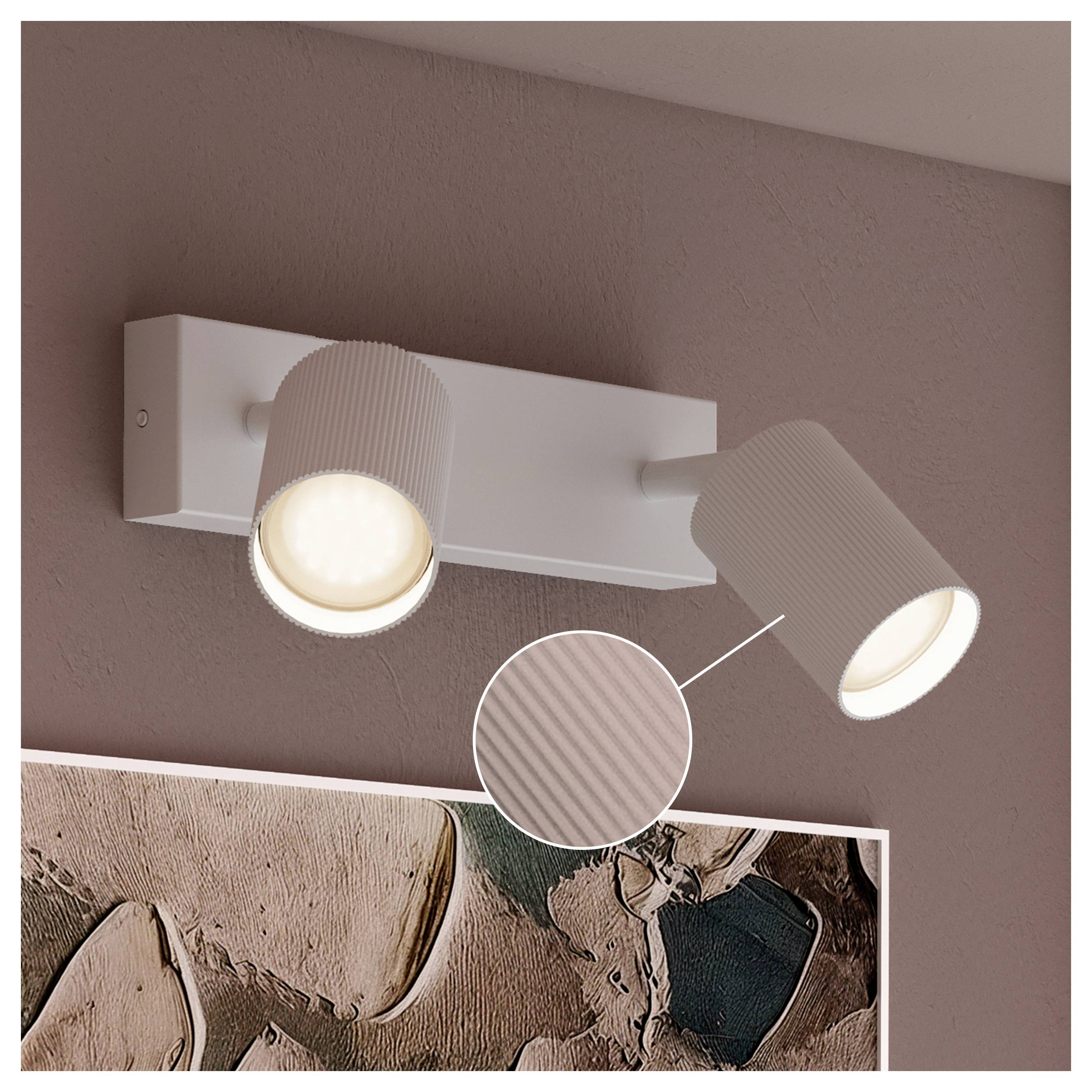 Two-head wall spotlight fixture in white, with both adjustable lamps lit above wall art on a mauve wall.