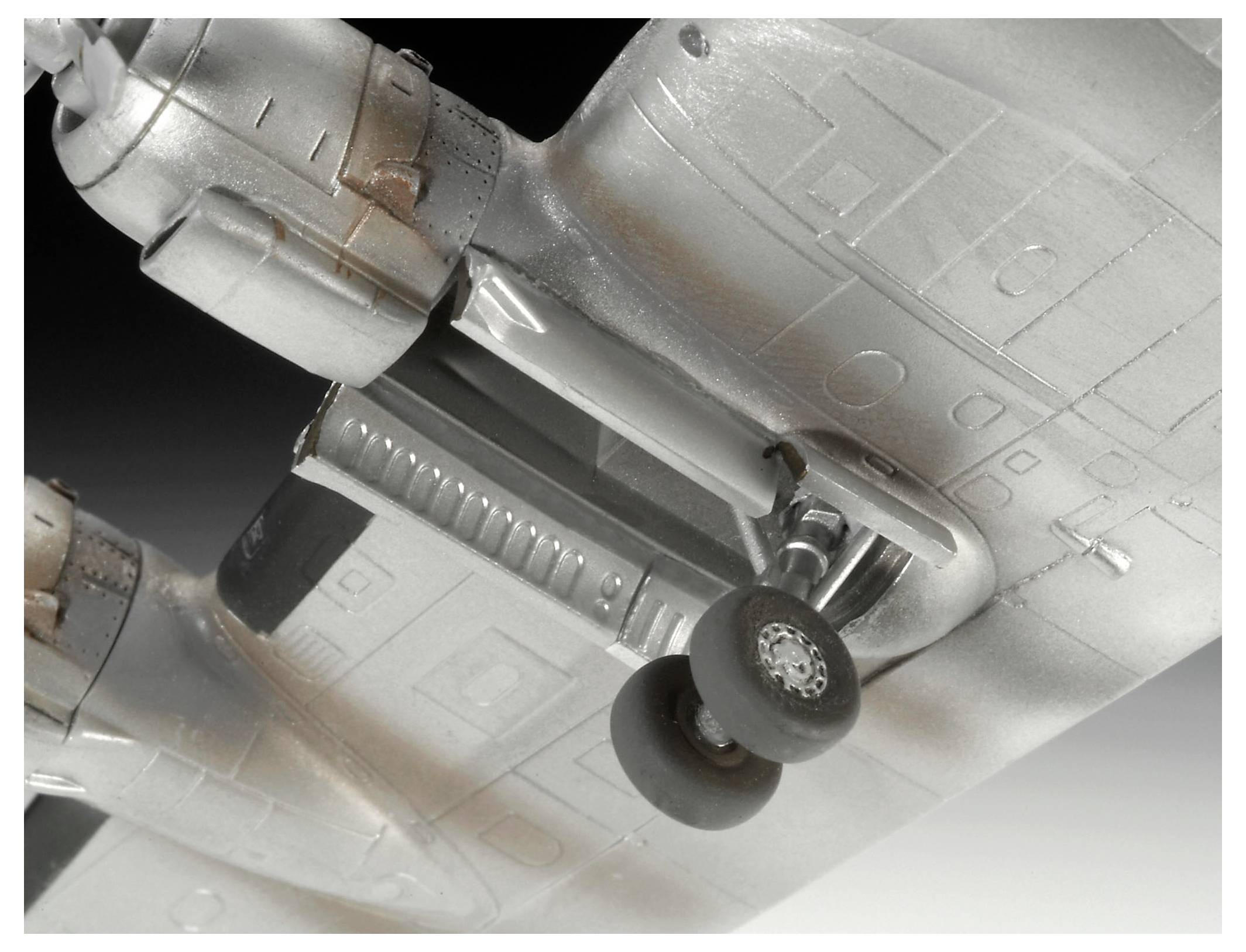 Close-up of a model airplane’s underside, showing landing gear and twin engine nacelles against a plain background.