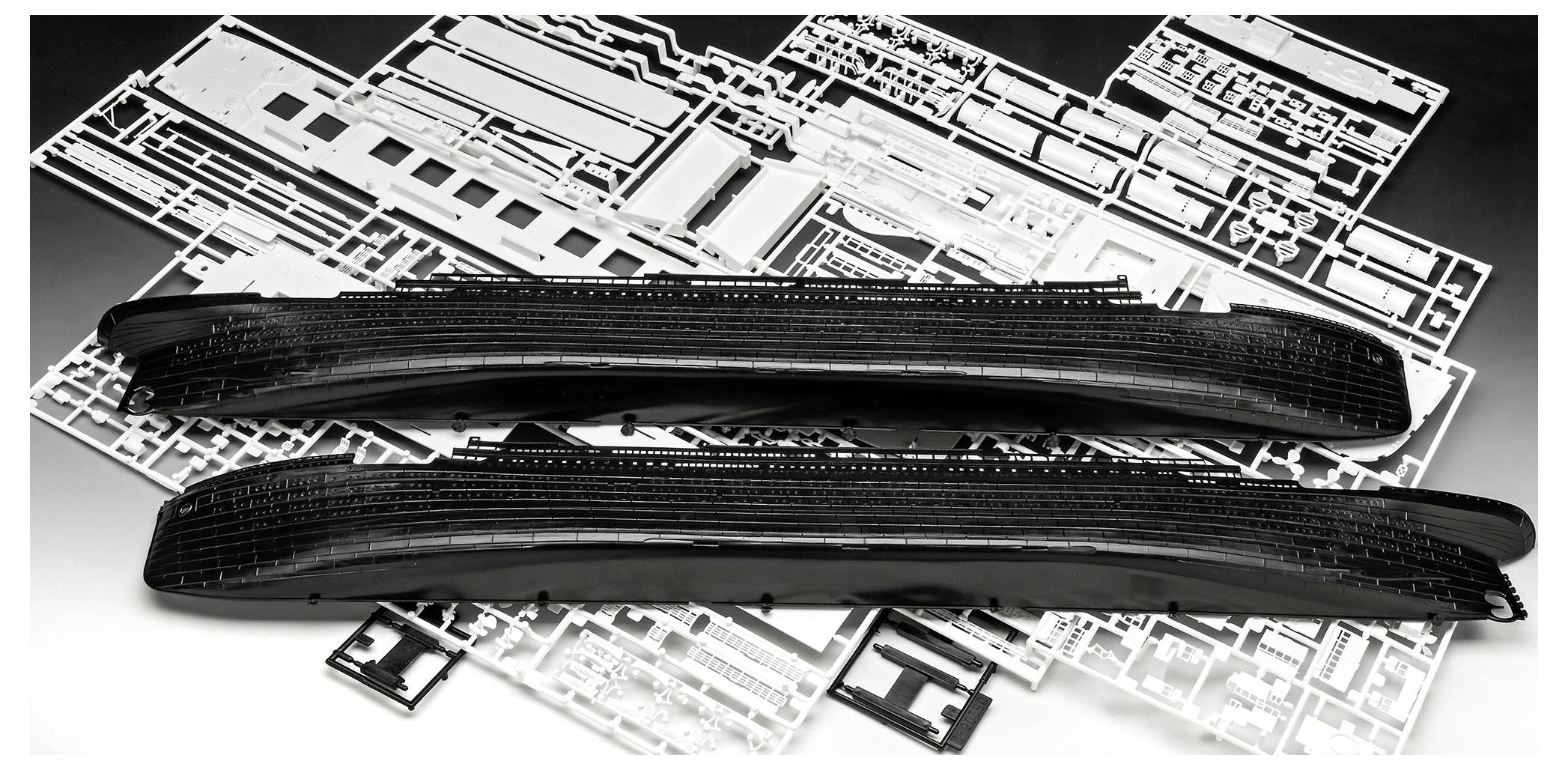 Two long black train body shells resting on white model train parts on a work surface.