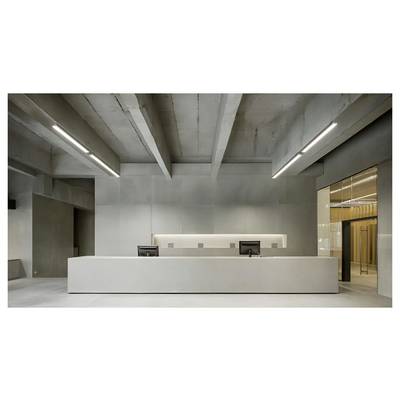 Modern minimalist reception desk in a concrete interior with two computer monitors and a lit doorway on the right.
