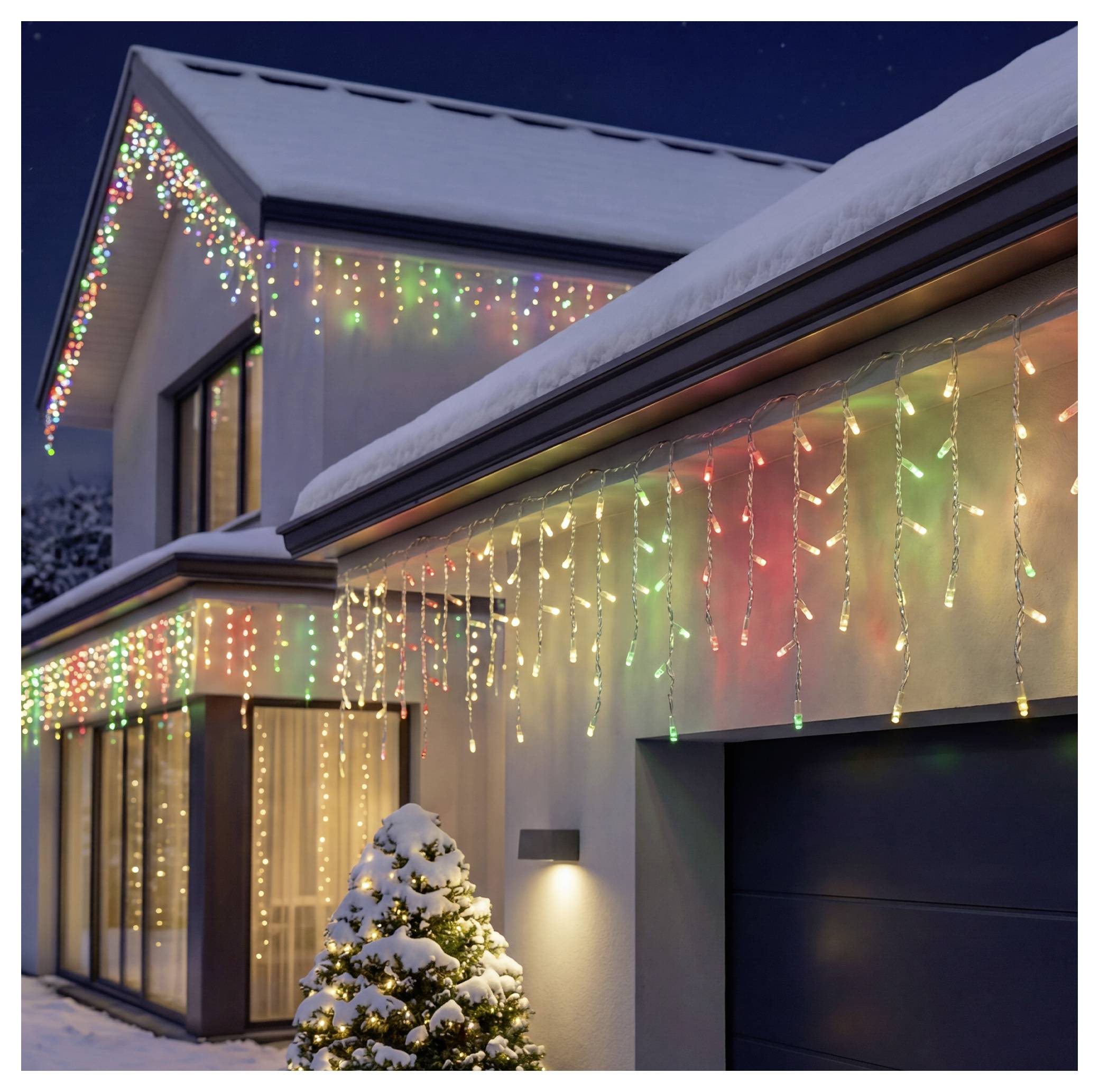 Snow-covered house decorated with colorful Christmas lights and icicle string lights, with a lit outdoor tree by the garage at night.