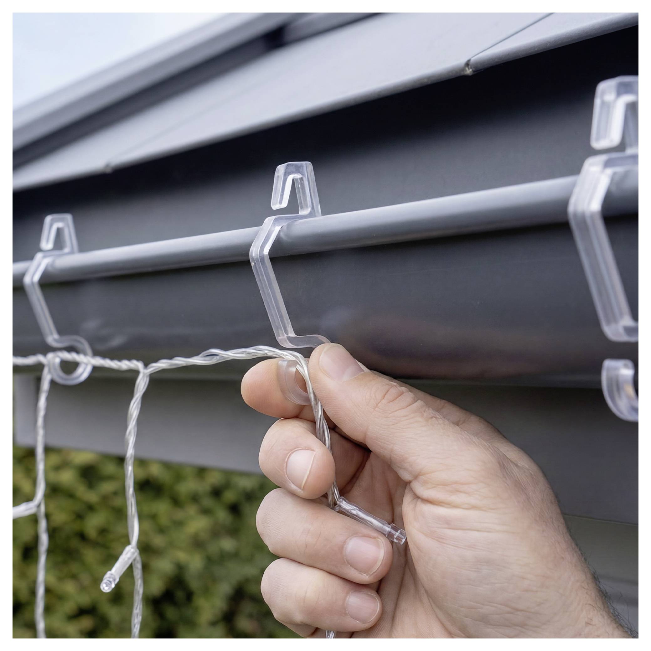 Hand clipping a string of outdoor lights onto a rain gutter under a roof edge.