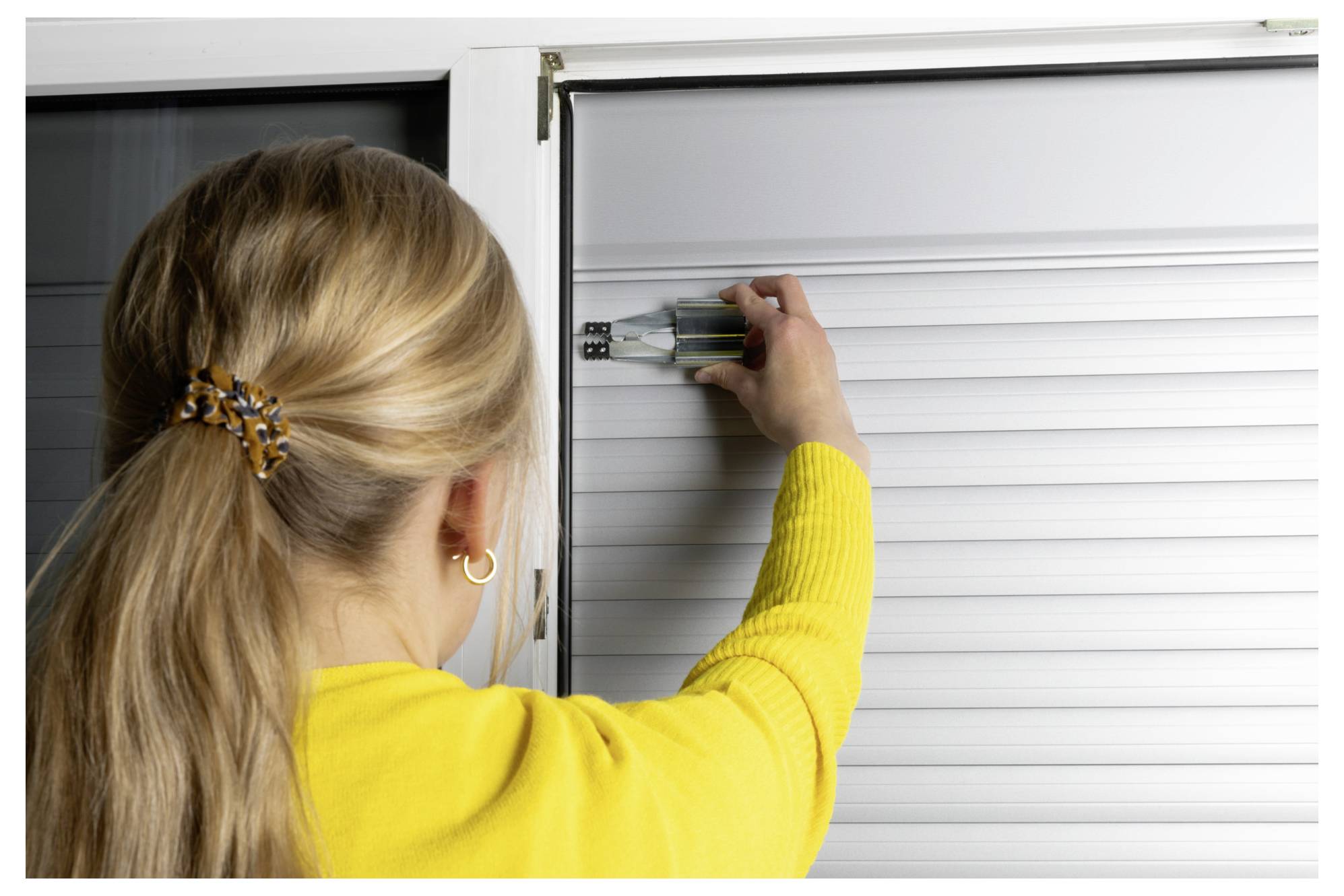 Woman in a yellow sweater uses a screwdriver to adjust the lock on a white roller shutter door.