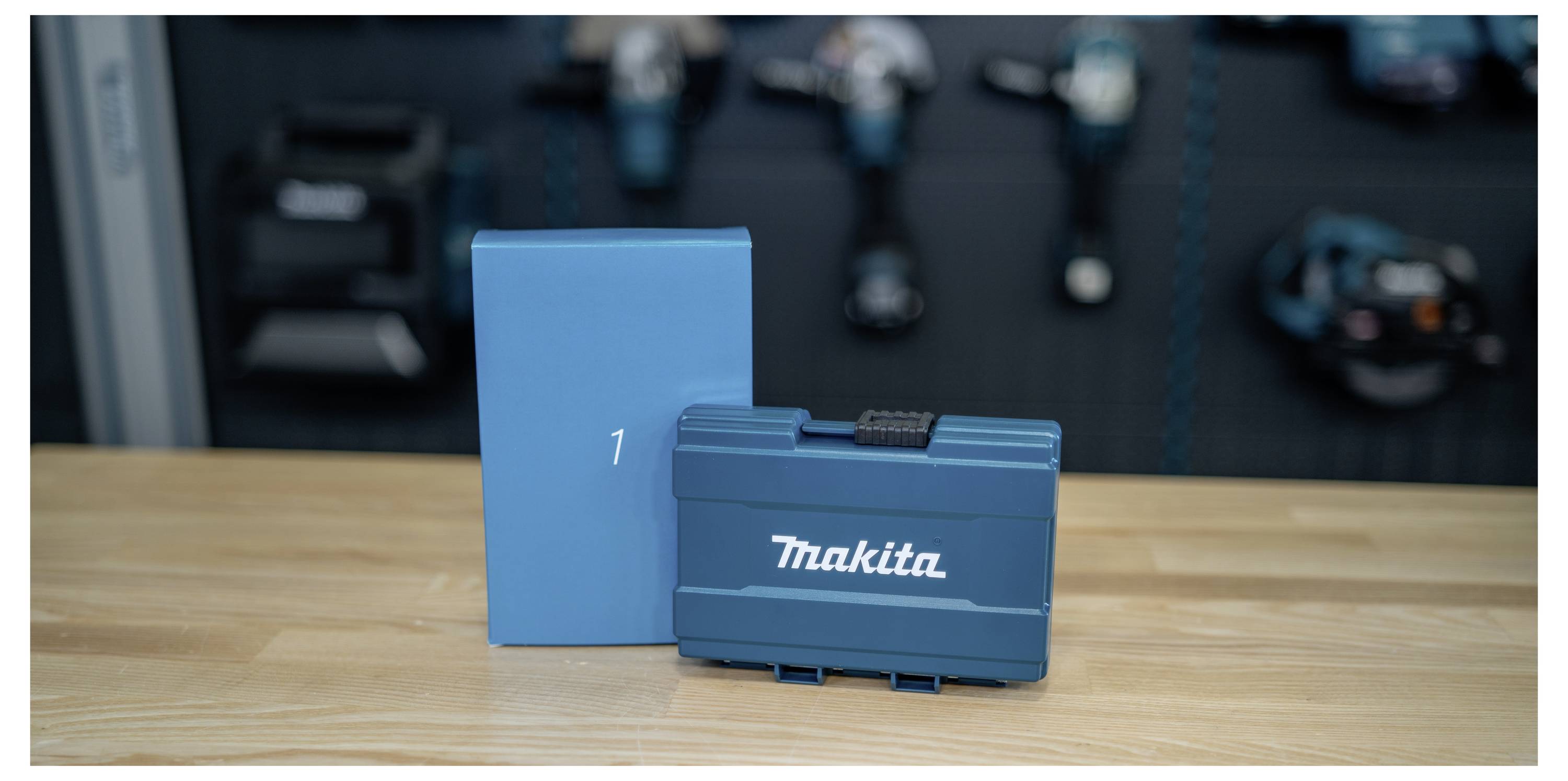Blue Makita tool case and matching box on a wooden table, with blurred power tools in the background.