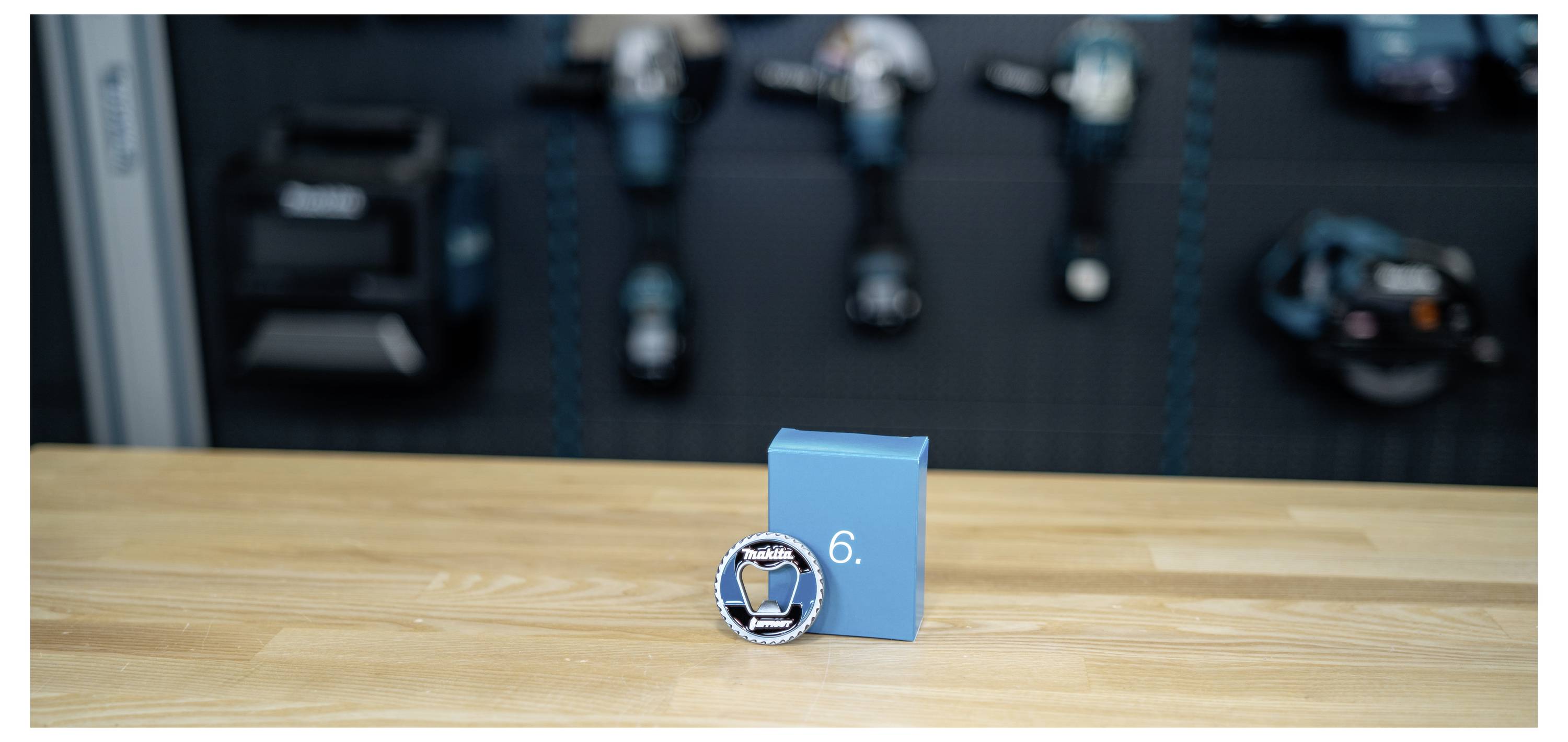 Blue award box with a round silver-and-blue medal marked 6 on a wooden table, with blurred exercise equipment in the background.