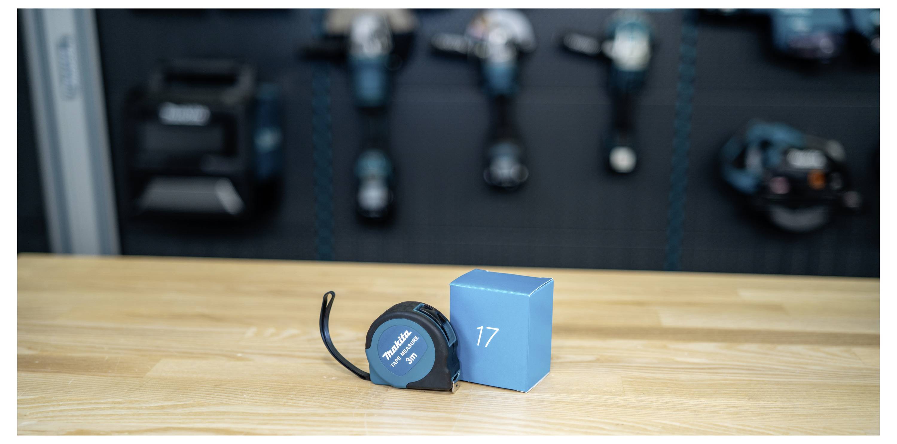 A blue tape measure next to a blue block marked '17' on a wooden table, with blurred gym equipment in the background.