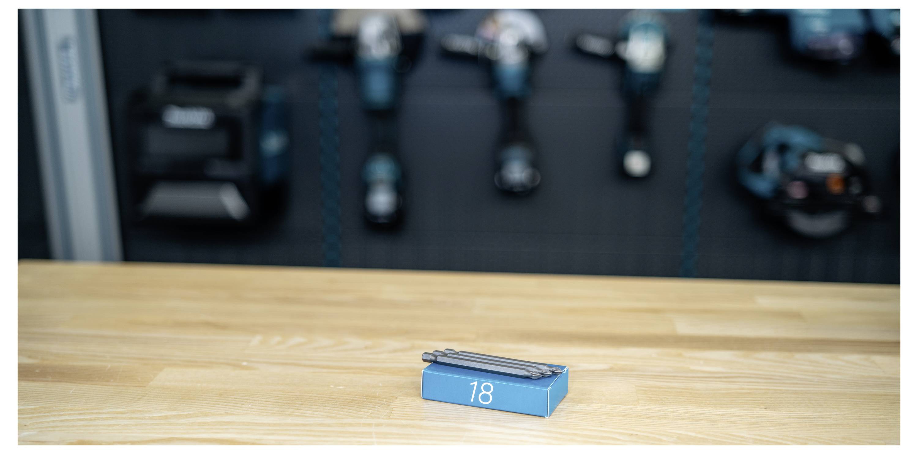 Blue matchbox labeled '18' on a wooden table, with a blurred overhead view of train tracks and small vehicles in the background.