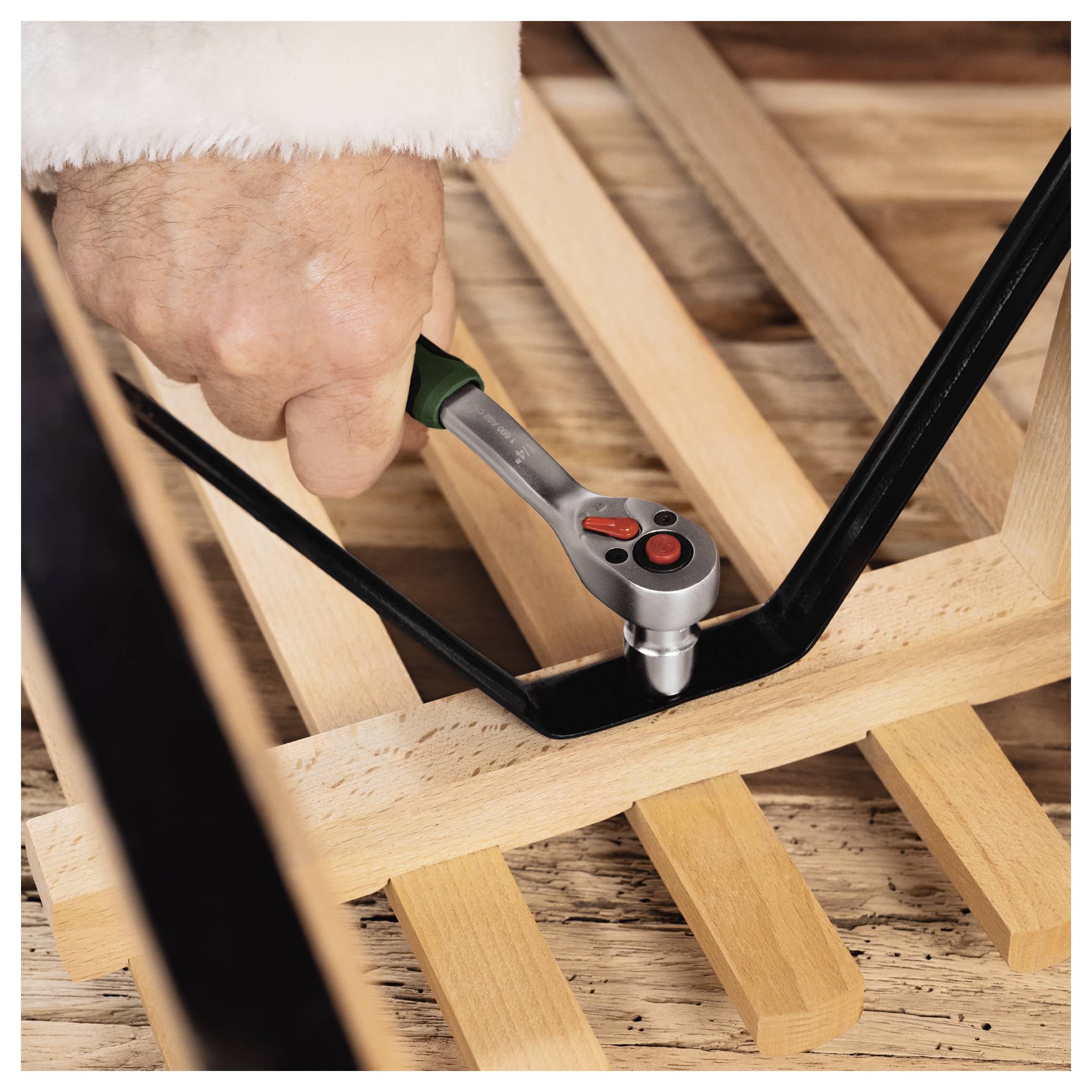 Close-up of a hand using a ratchet wrench to tighten a black metal frame on a wooden structure.