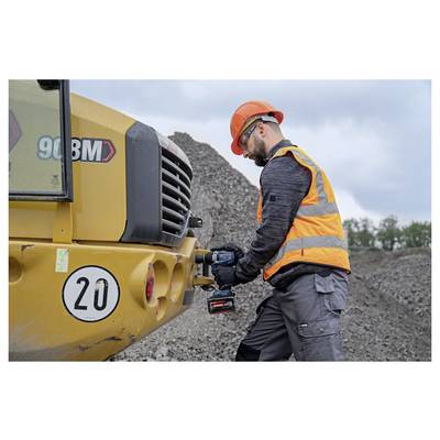 Construction worker in orange safety gear using a power drill on a yellow machine at a gravel worksite.