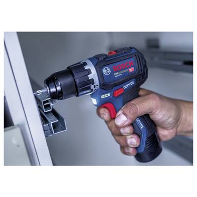 Hand holding a Bosch cordless drill driving a screw into a metal bracket on a light gray surface.