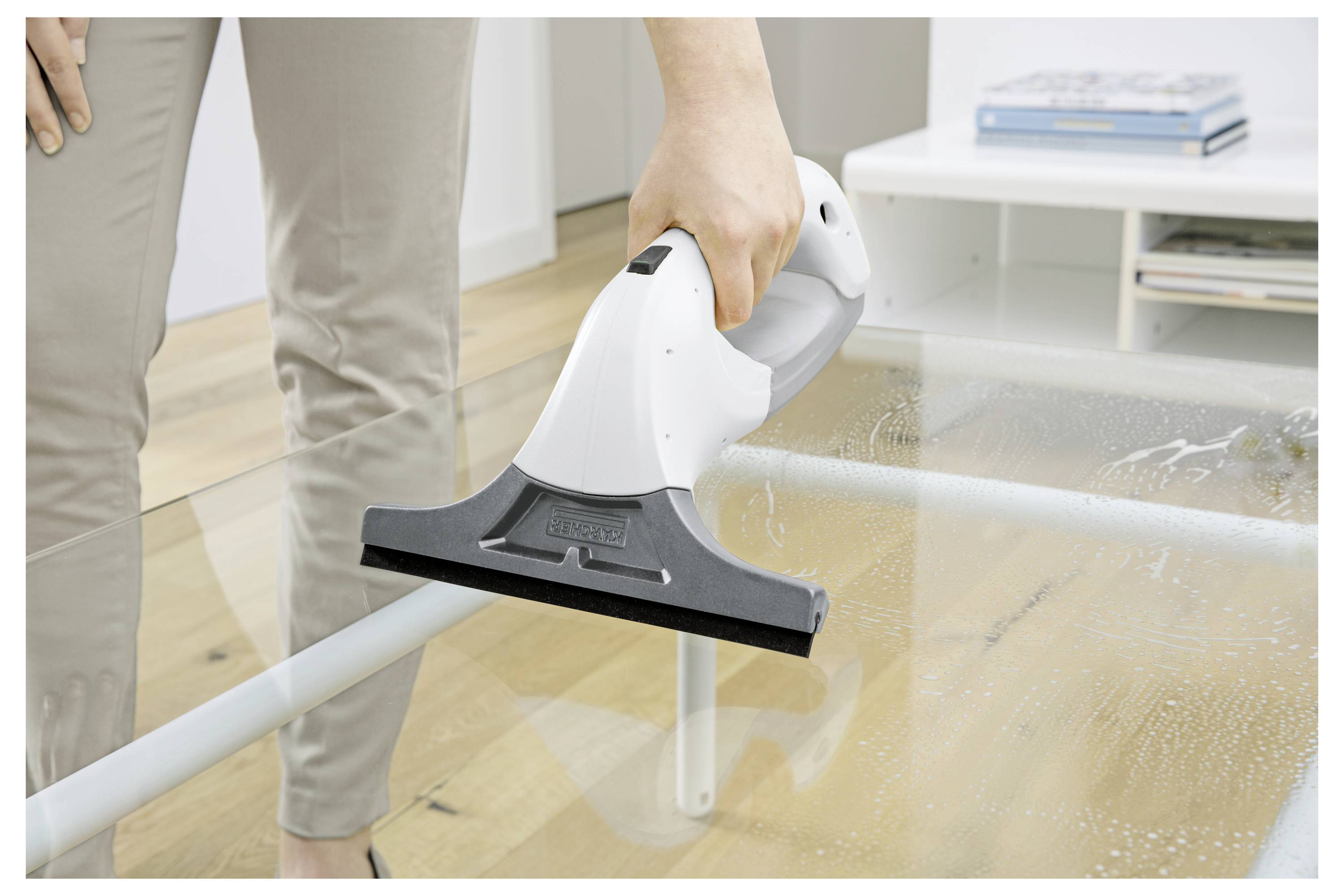 Person using a handheld vacuum to clean a glass tabletop, with water droplets being suctioned away in a home interior.