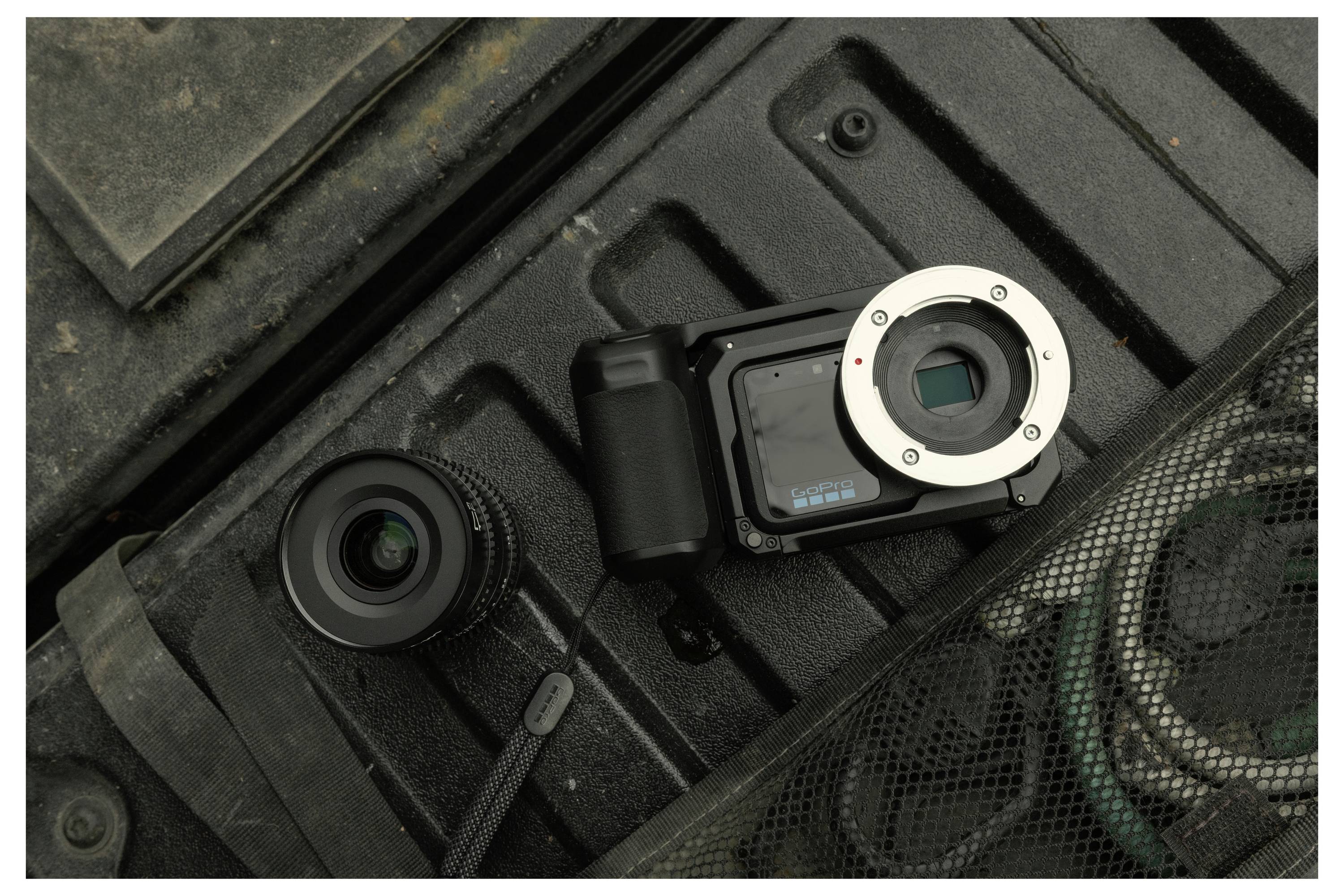 Two camera lenses and a mirrorless camera body rest in a foam-lined case, with a mesh pocket and strap visible nearby.