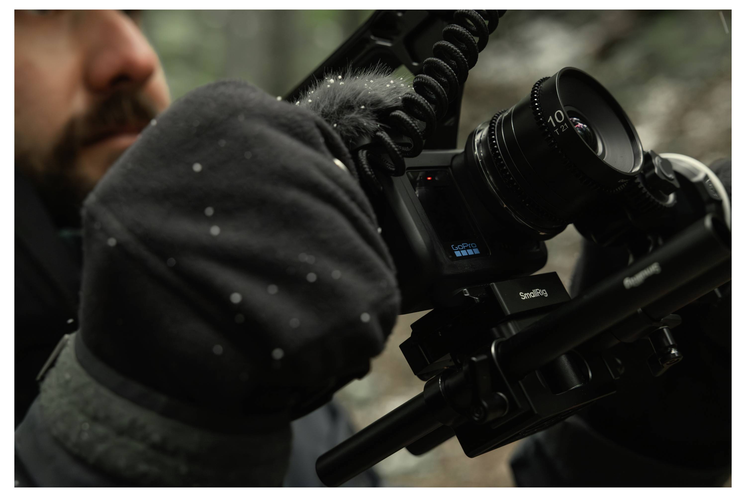 Close-up of a person filming with a professional video camera mounted on a rig, showing a gloved hand adjusting the equipment.