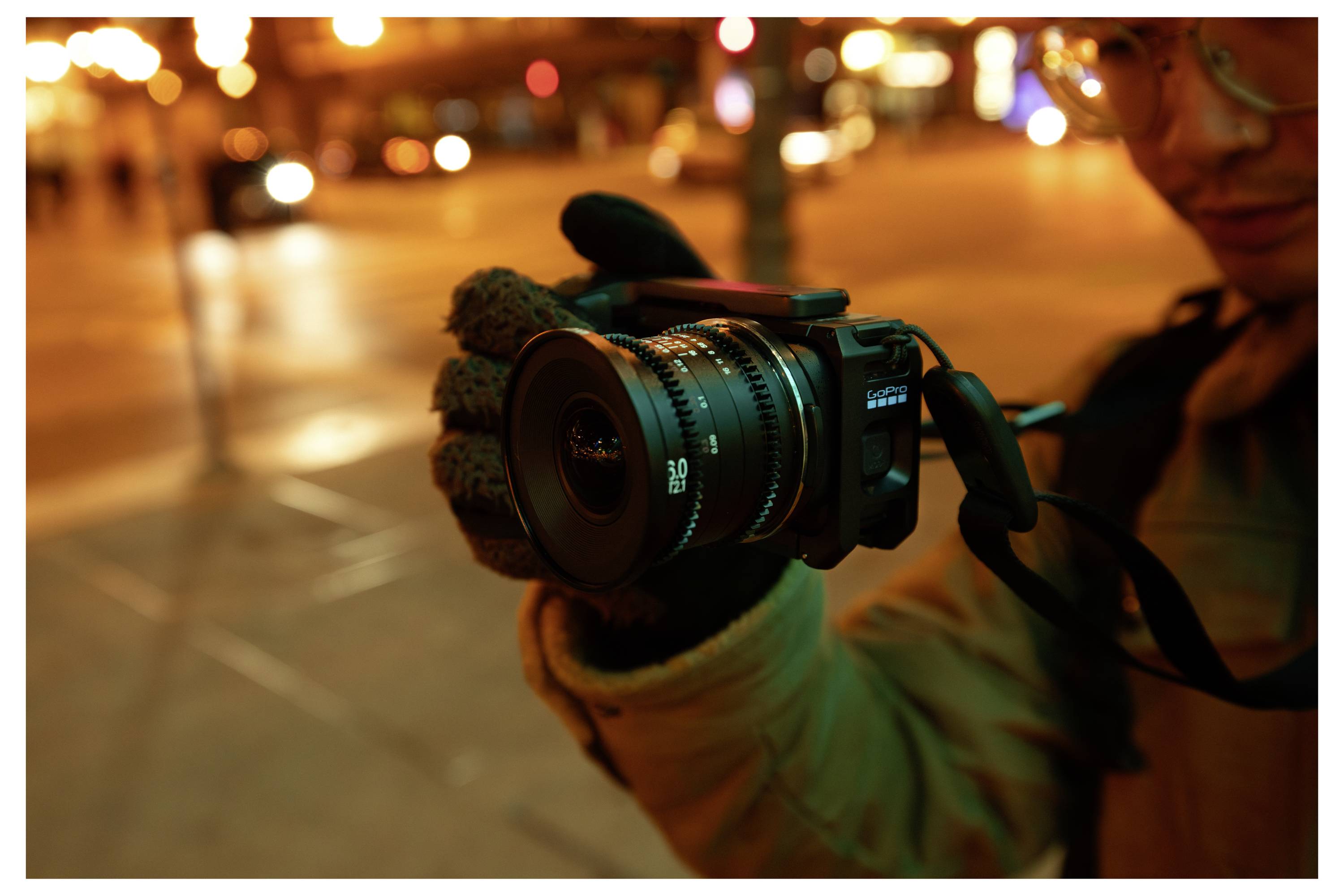 Person holding a camera with a wide-angle lens at night on a city street, with blurred traffic lights in the background.