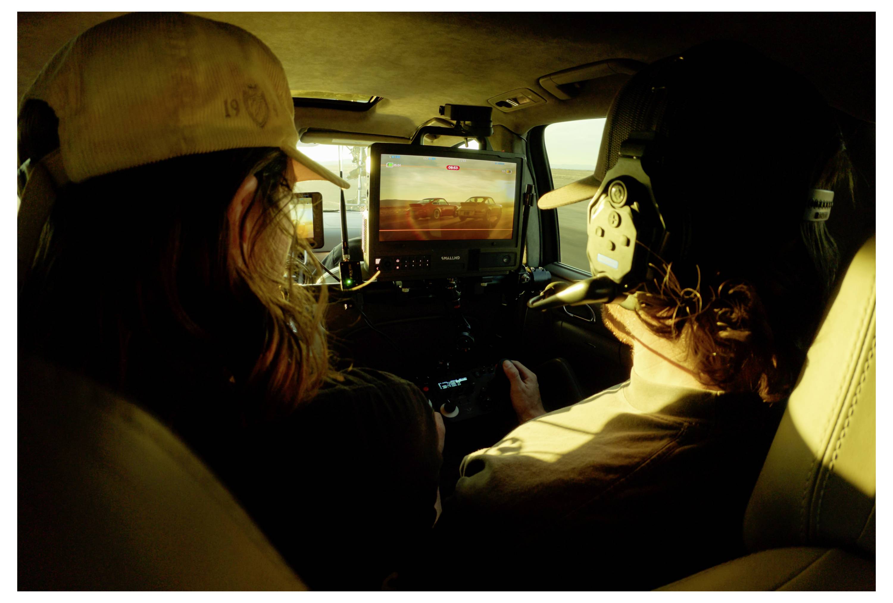 Two people sit in a small aircraft cockpit at sunset, with a front display showing a runway or landing view.<br>