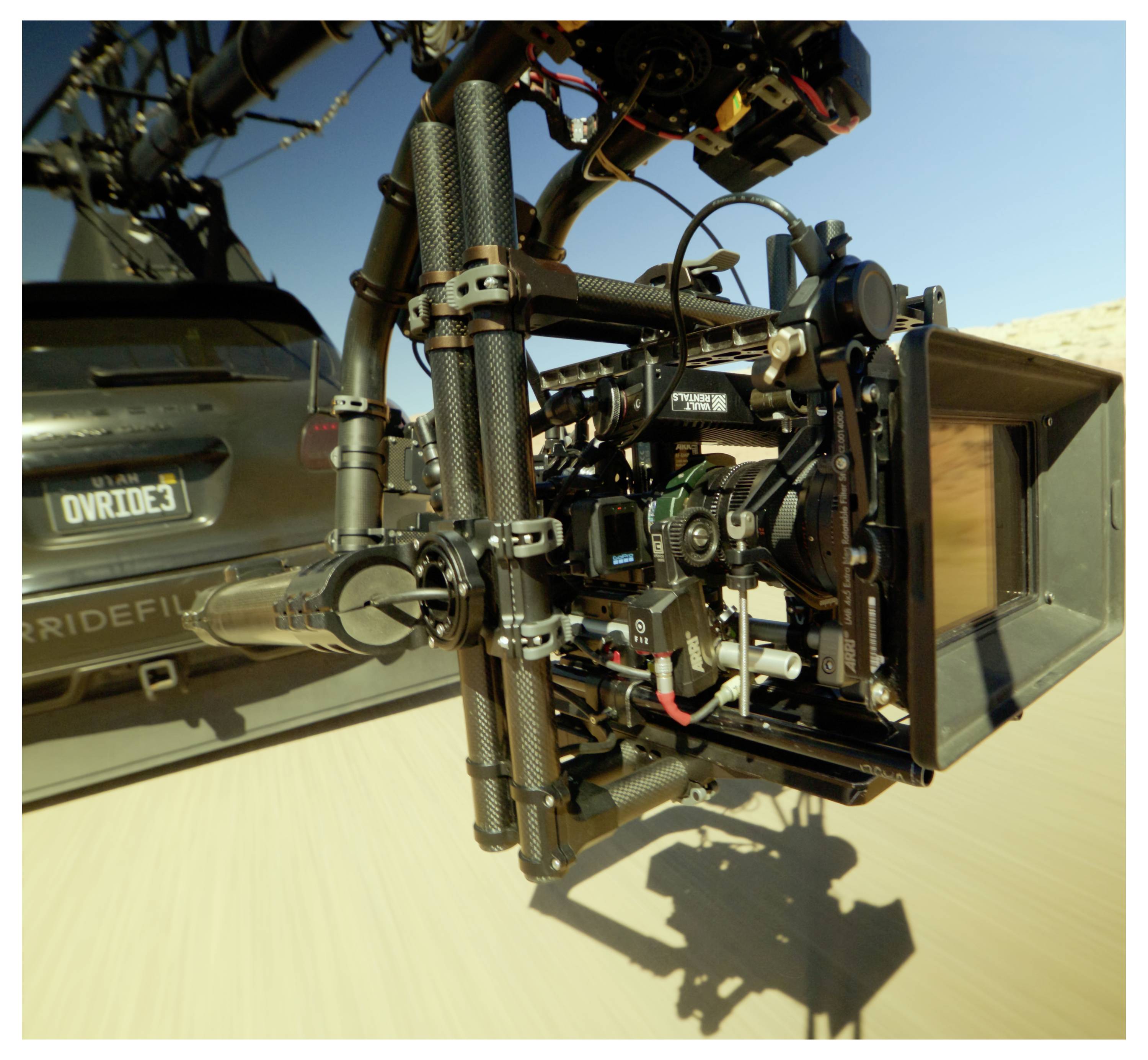 Close-up of a professional camera mounted on a drone, filming while flying over a sandy landscape.