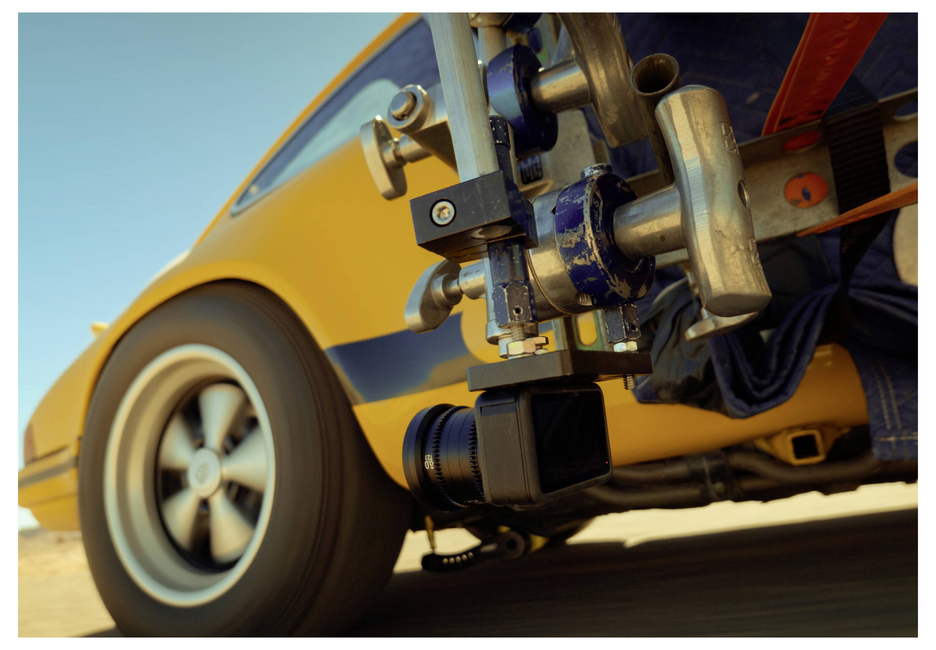 Close-up of a stabilized camera rig mounted to a moving yellow car, with the wheel and lower body visible.