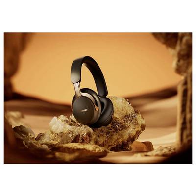 Black Bose over-ear headphones resting on a rock in a warm orange desert-like setting.