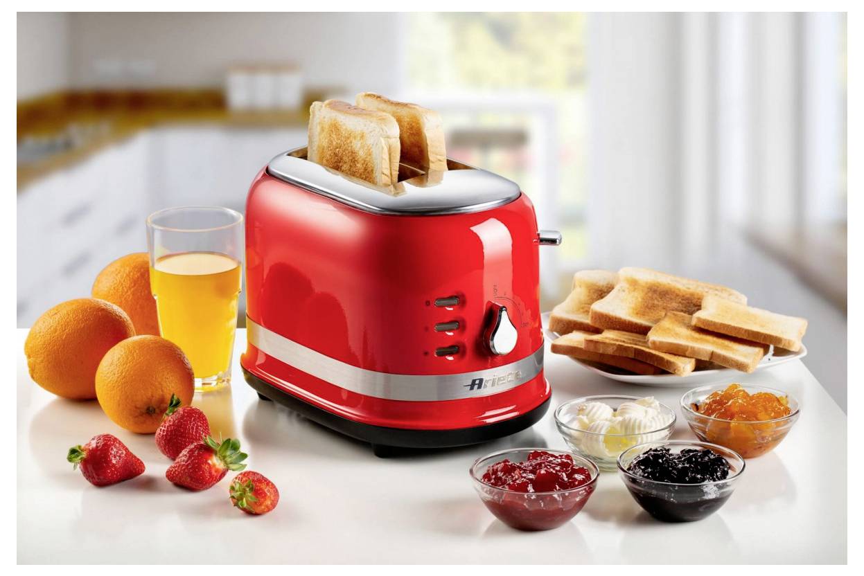 Red toaster with toast popping up, surrounded by oranges, strawberries, juice, and bowls of jam and butter on a kitchen counter.