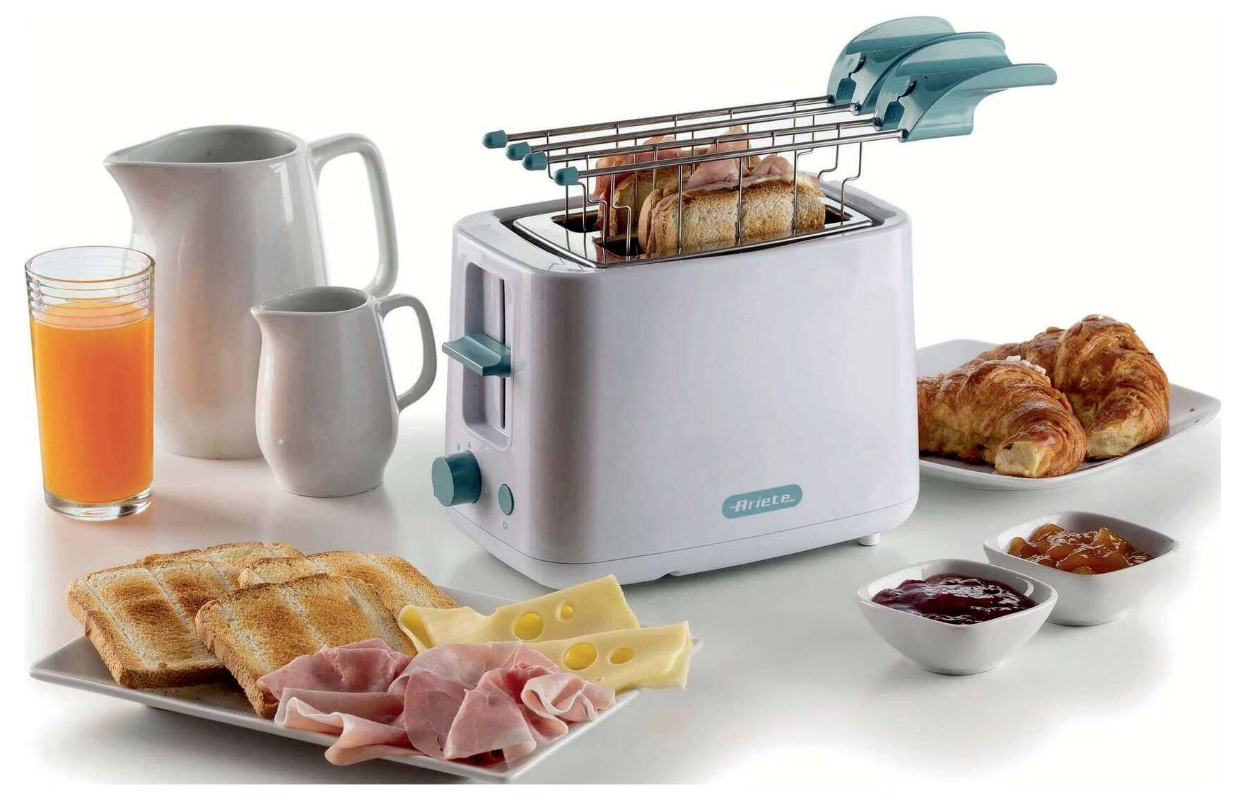 Kitchen toaster with toast and breakfast spread, including croissants, ham, cheese, jam, orange juice, and pitchers on a white surface.