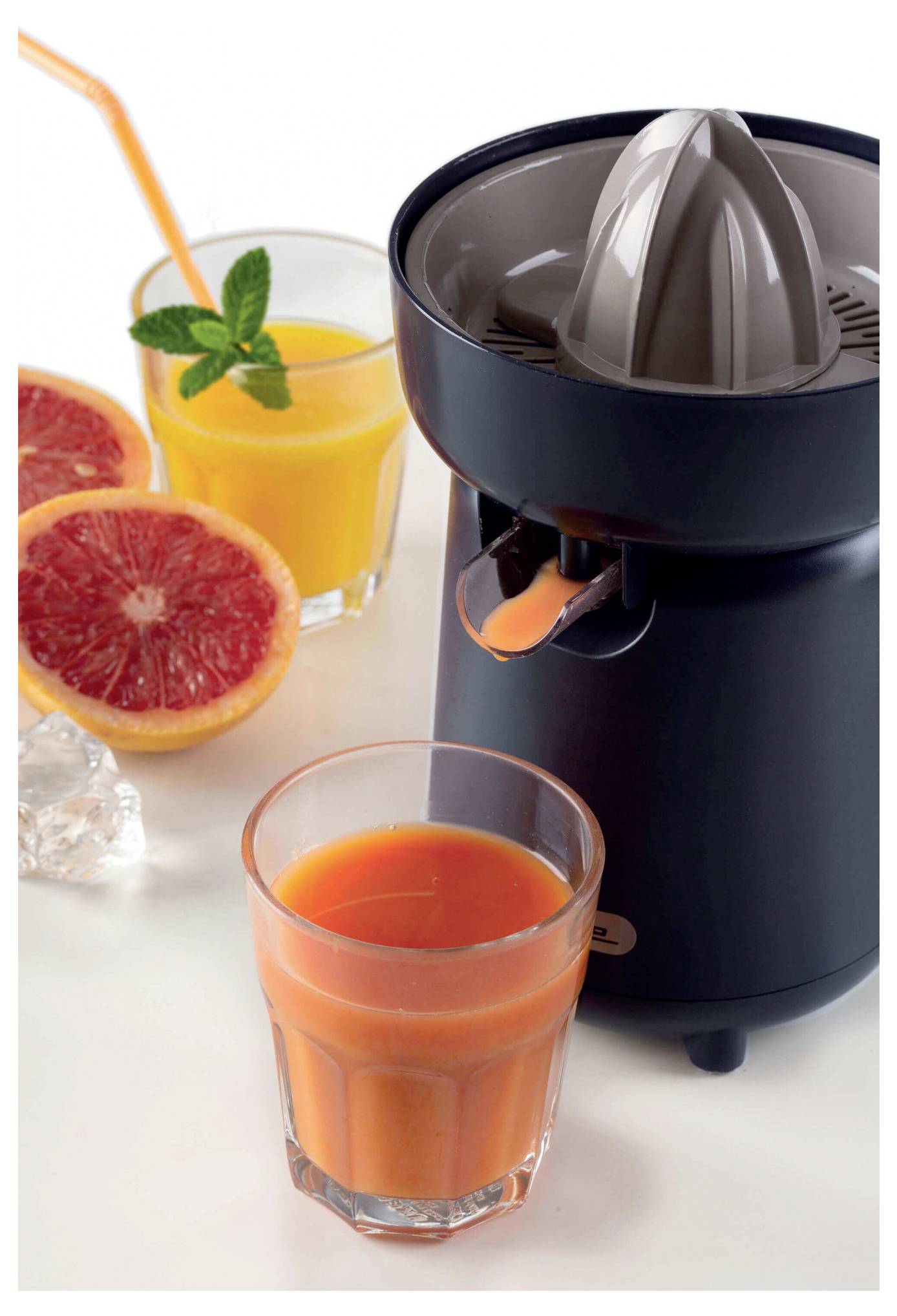 Countertop citrus juicer with freshly squeezed orange juice in a glass, two halved grapefruits, and a mint-garnished orange drink with a straw.