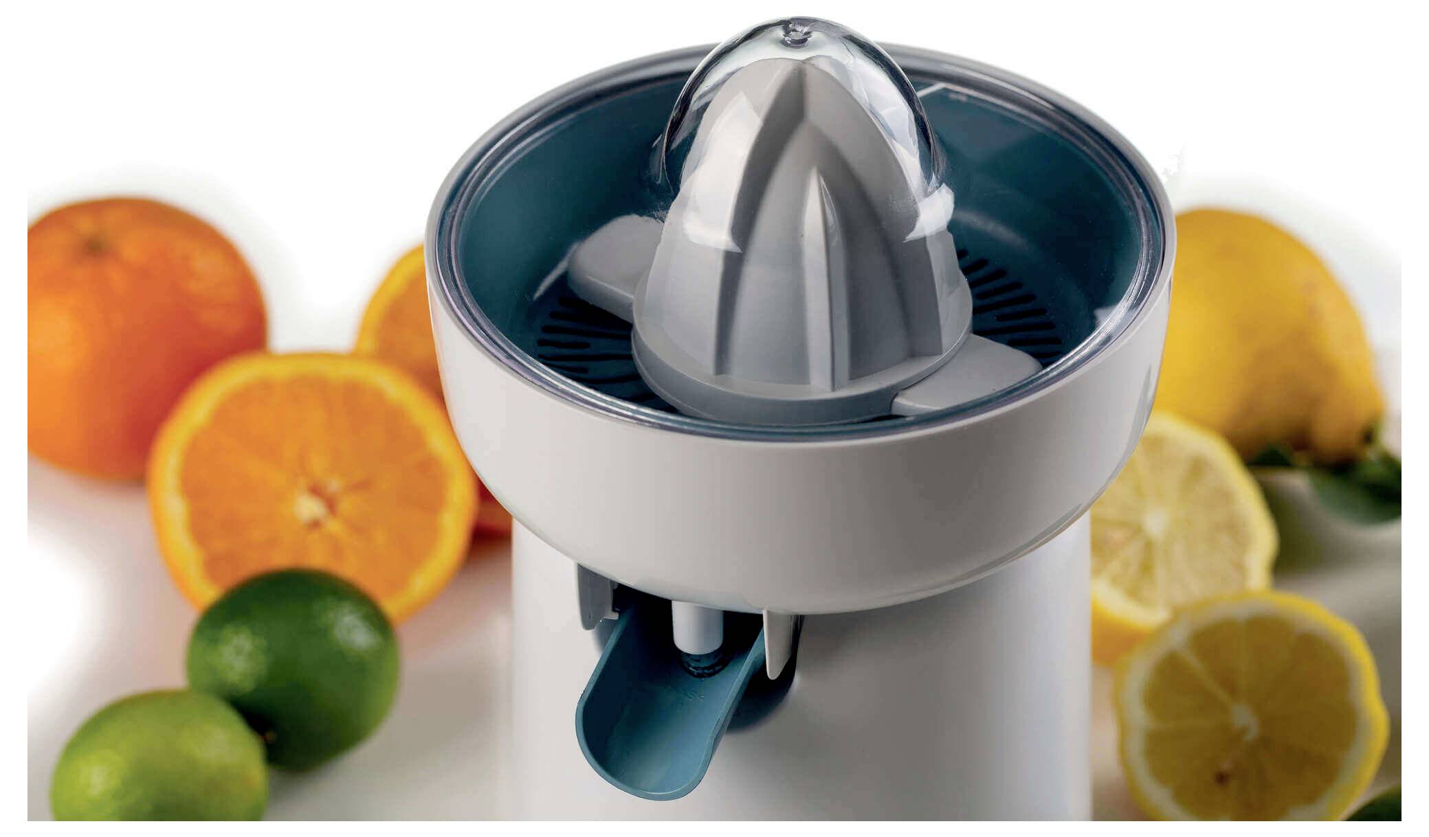 Electric citrus juicer centered on a countertop, surrounded by oranges, lemons, and limes with cut fruit showing fresh juice.