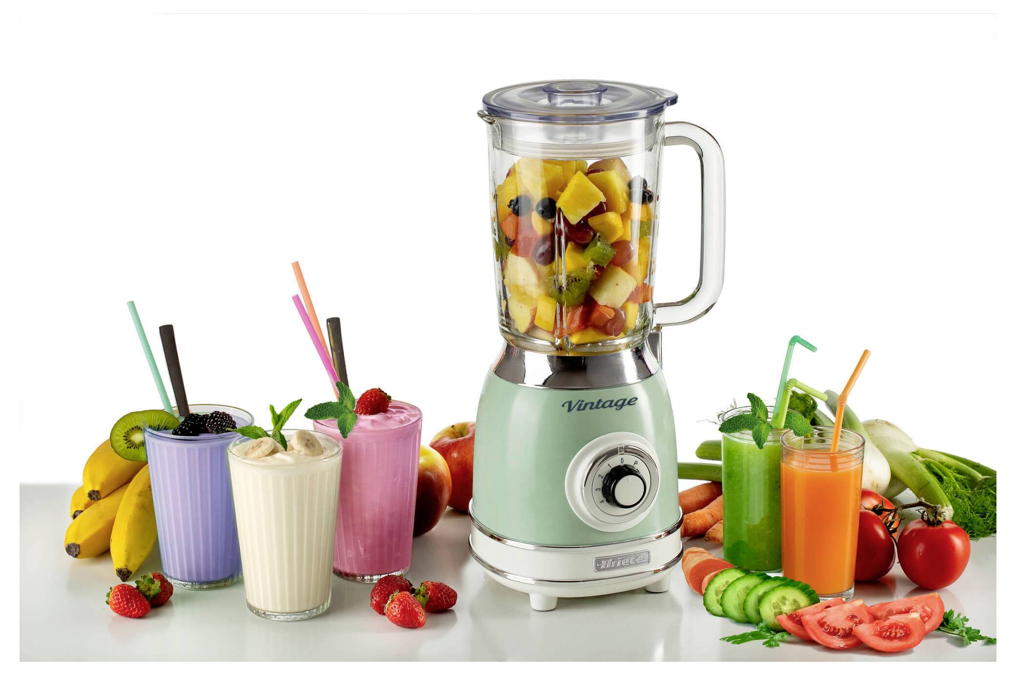 Mint green blender with fruit inside beside three smoothies and assorted fresh fruits and vegetables on a white background.