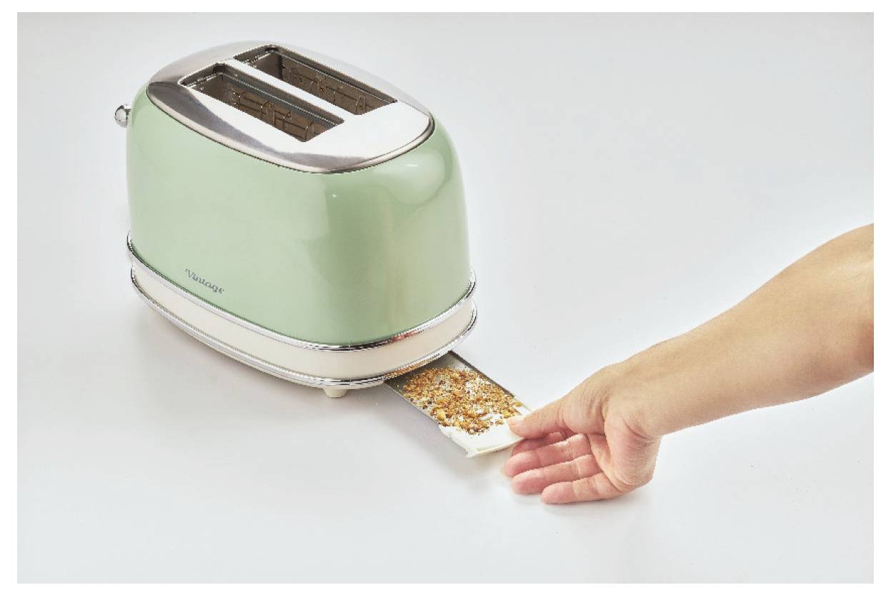 Hand placing a slice of bread with seeds into a green two-slice toaster.