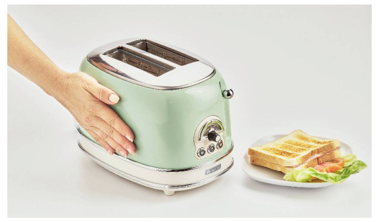 A hand presses down on a mint-green toaster beside a plate of toasted bread and lettuce, showing breakfast preparation.