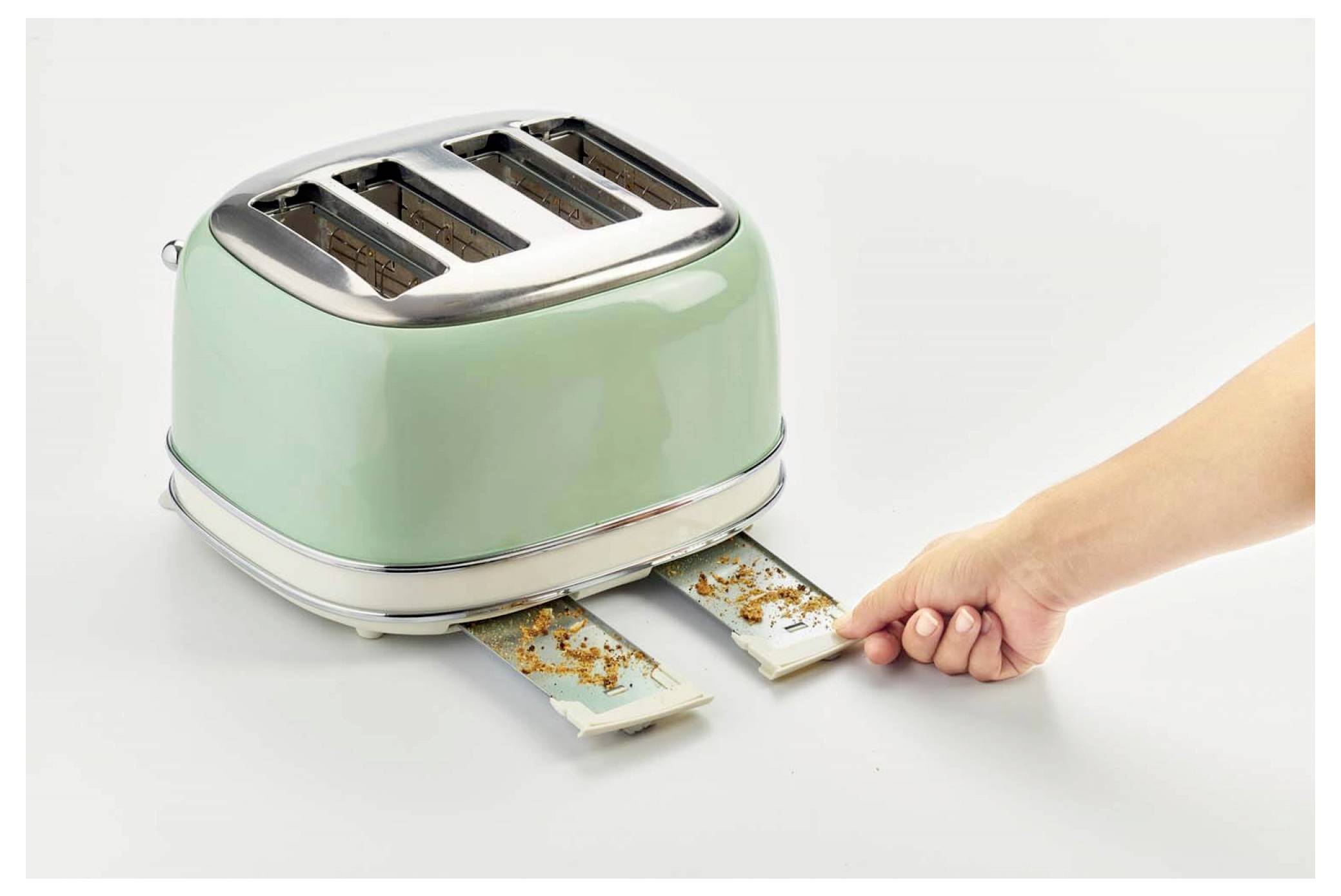 Hand pulling out a jammed toast slice from a green two-slot toaster with crumbs spilling out.