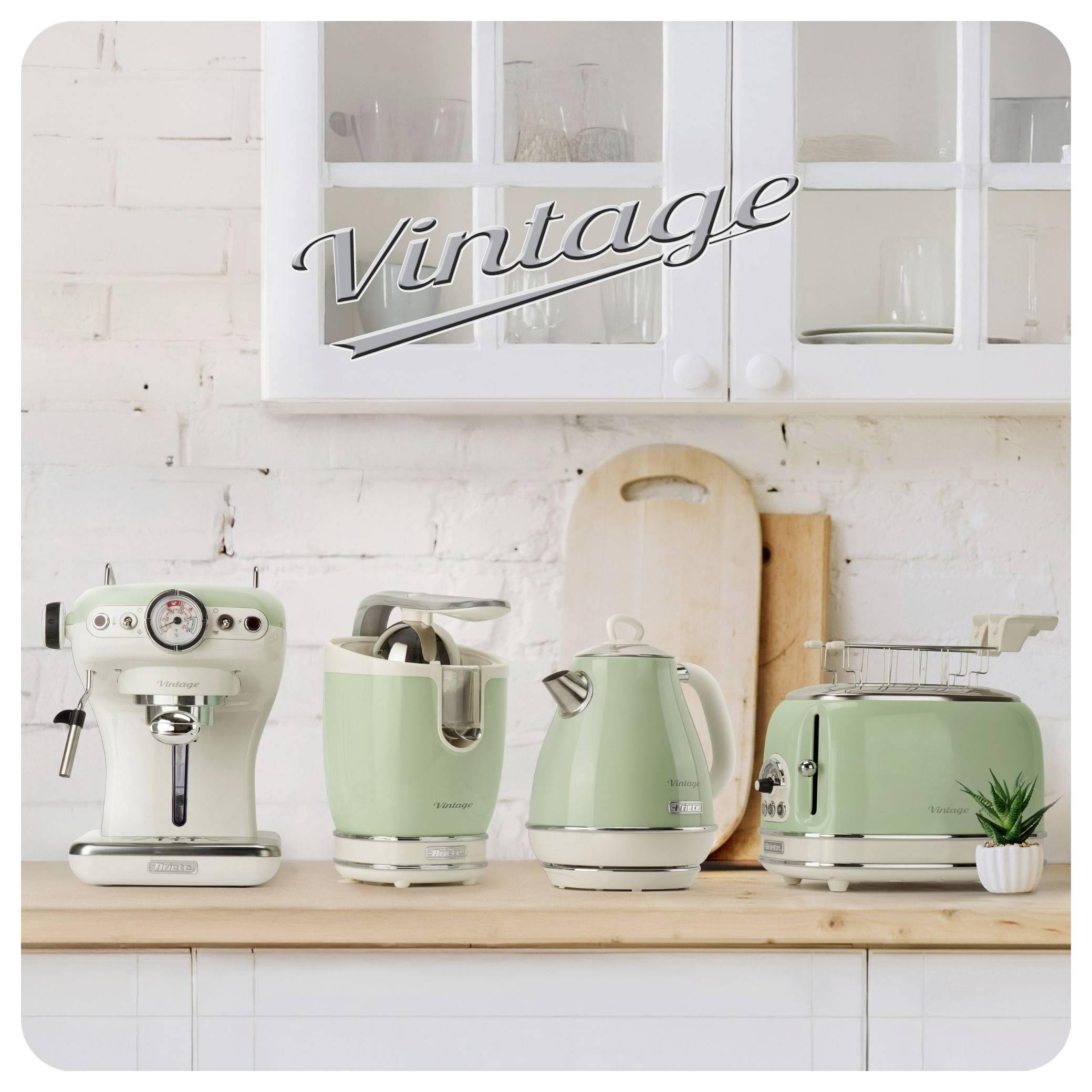 Vintage-style kitchen display with mint-green espresso machine, kettle, toaster, and blender on a wooden counter beneath white cabinets.