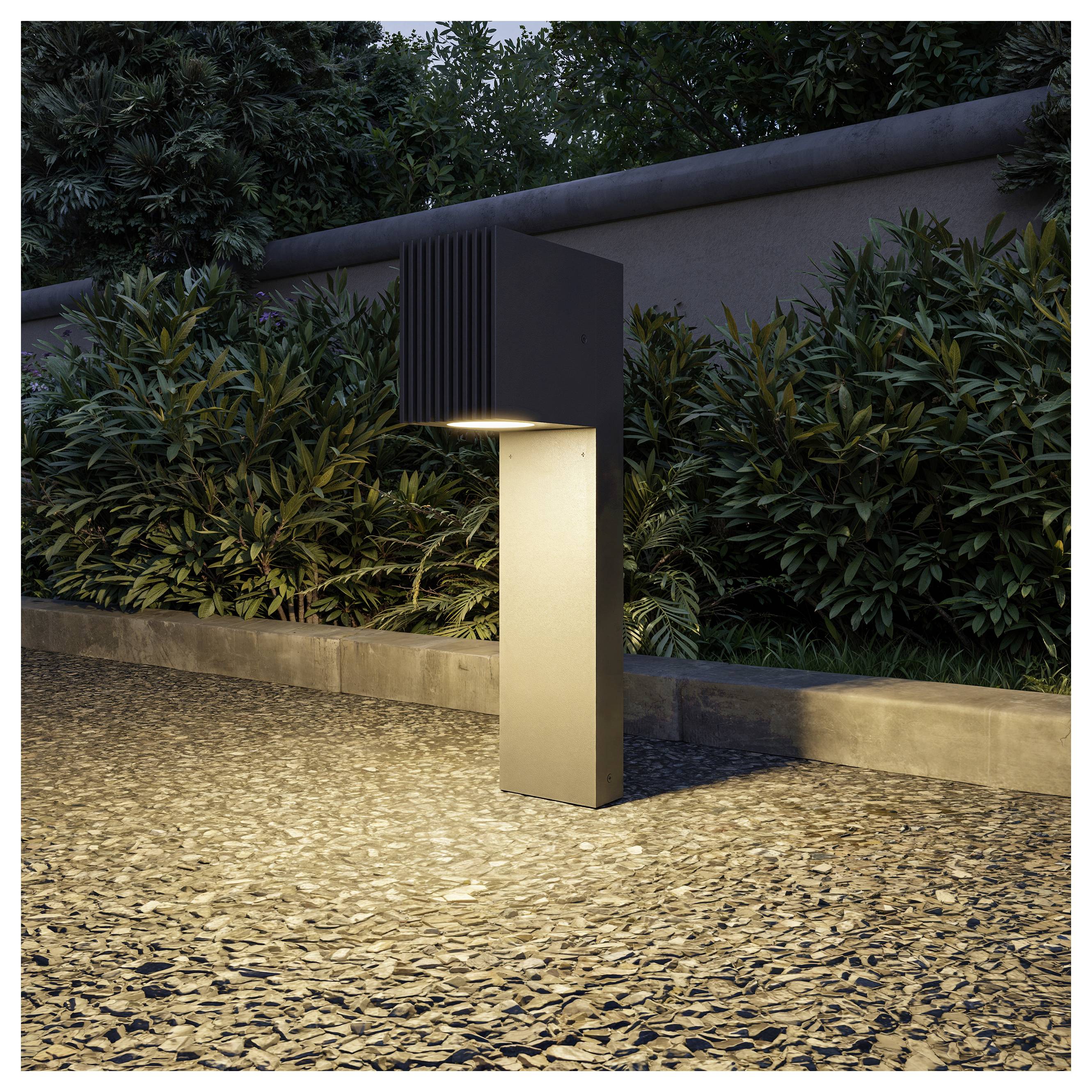 Modern outdoor path light with a dark rectangular top and glowing downlight, illuminating a pebble path beside a landscaped garden at dusk.