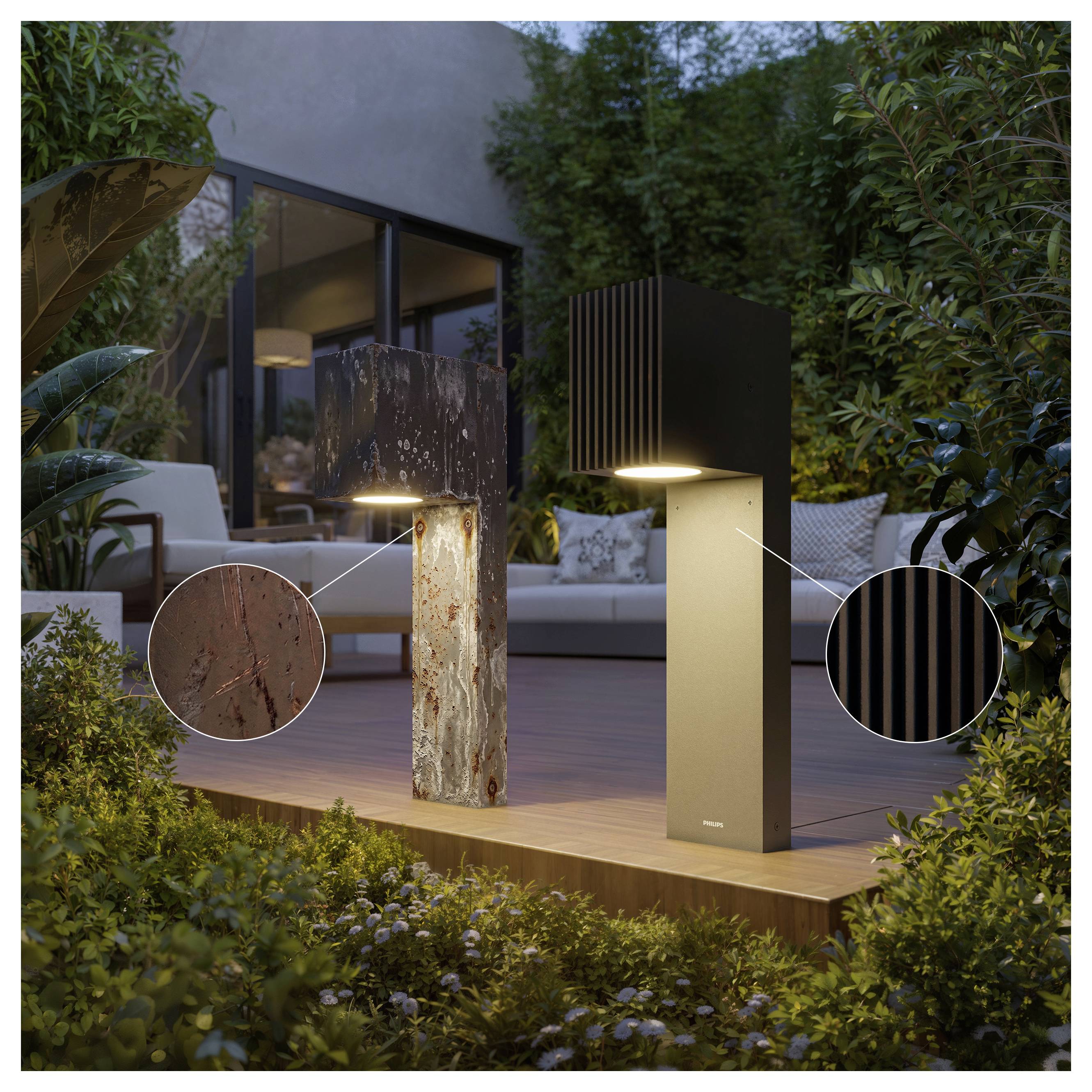 Two outdoor pathway lights on a wooden deck, showing weathered rusted and matte black finishes with close-up detail circles.