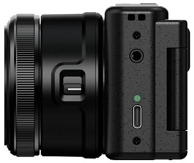 Side view of a compact black camera with a large lens, textured grip, shutter button, indicator light, and a side hinge or accessory attachment.